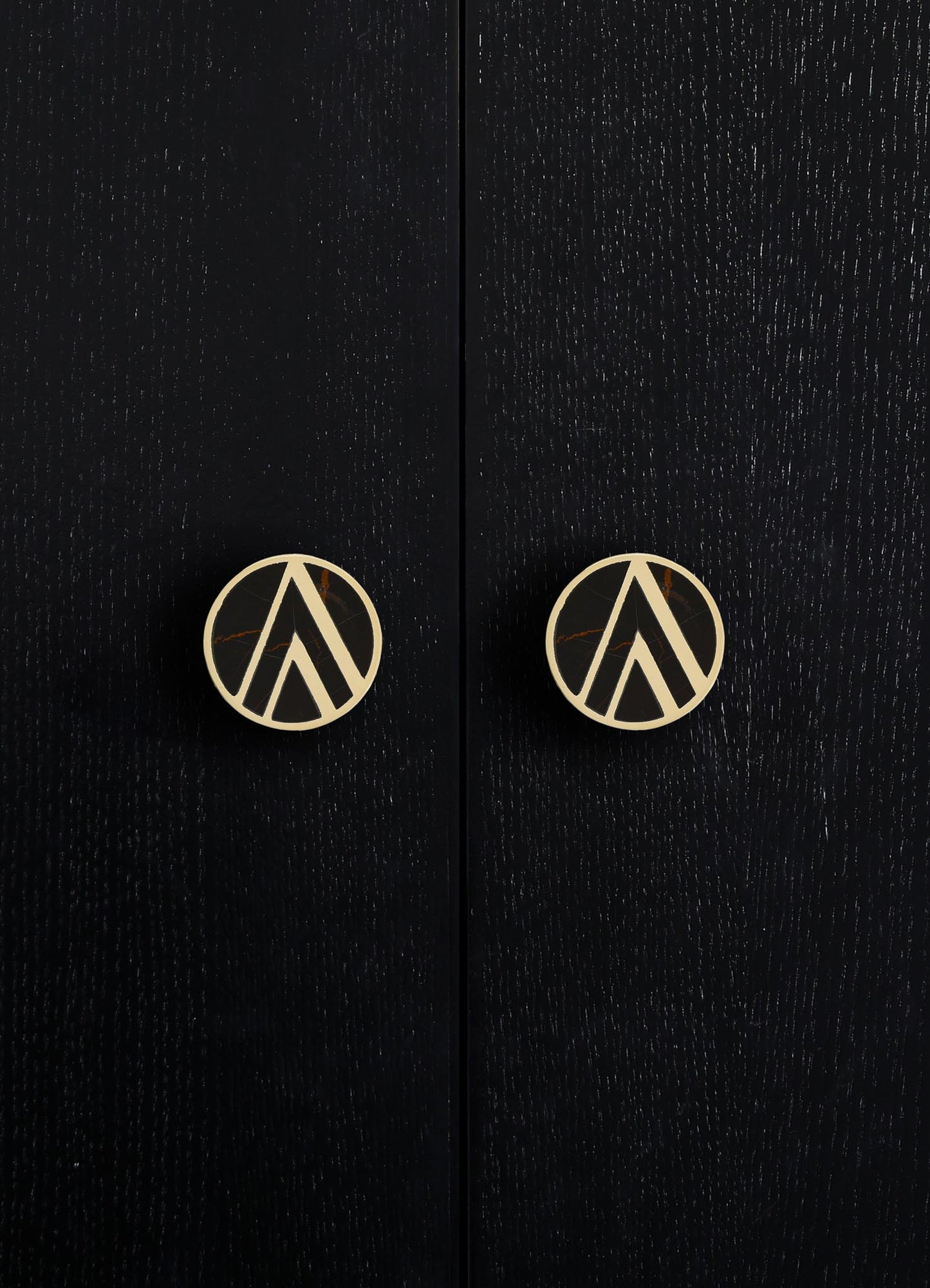 Black wooden cabinet with a textured finish and round brass knobs featuring a geometric cutout pattern.