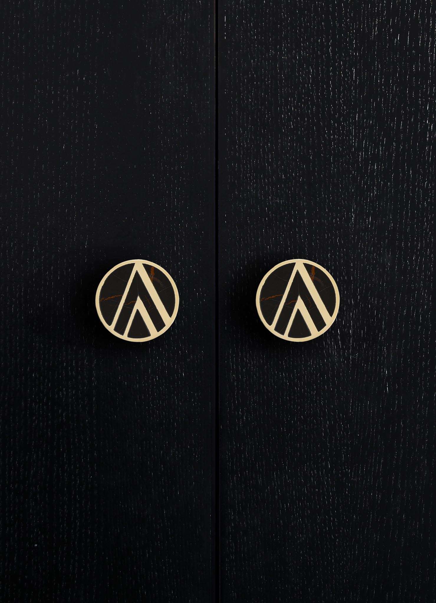 Black wooden cabinet with a textured finish and round brass knobs featuring a geometric cutout pattern.