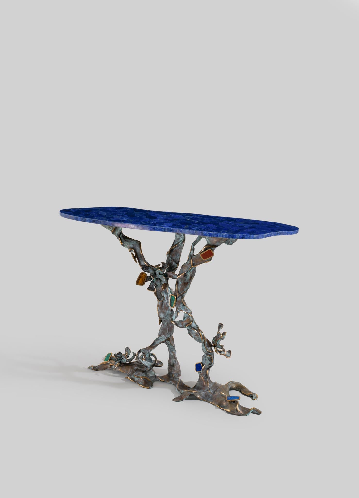A side table with a blue mosaic top and an intricate, sculptural metal base featuring organic, flowing forms with colorful inlays. The design combines contemporary artistry with a natural-inspired aesthetic.