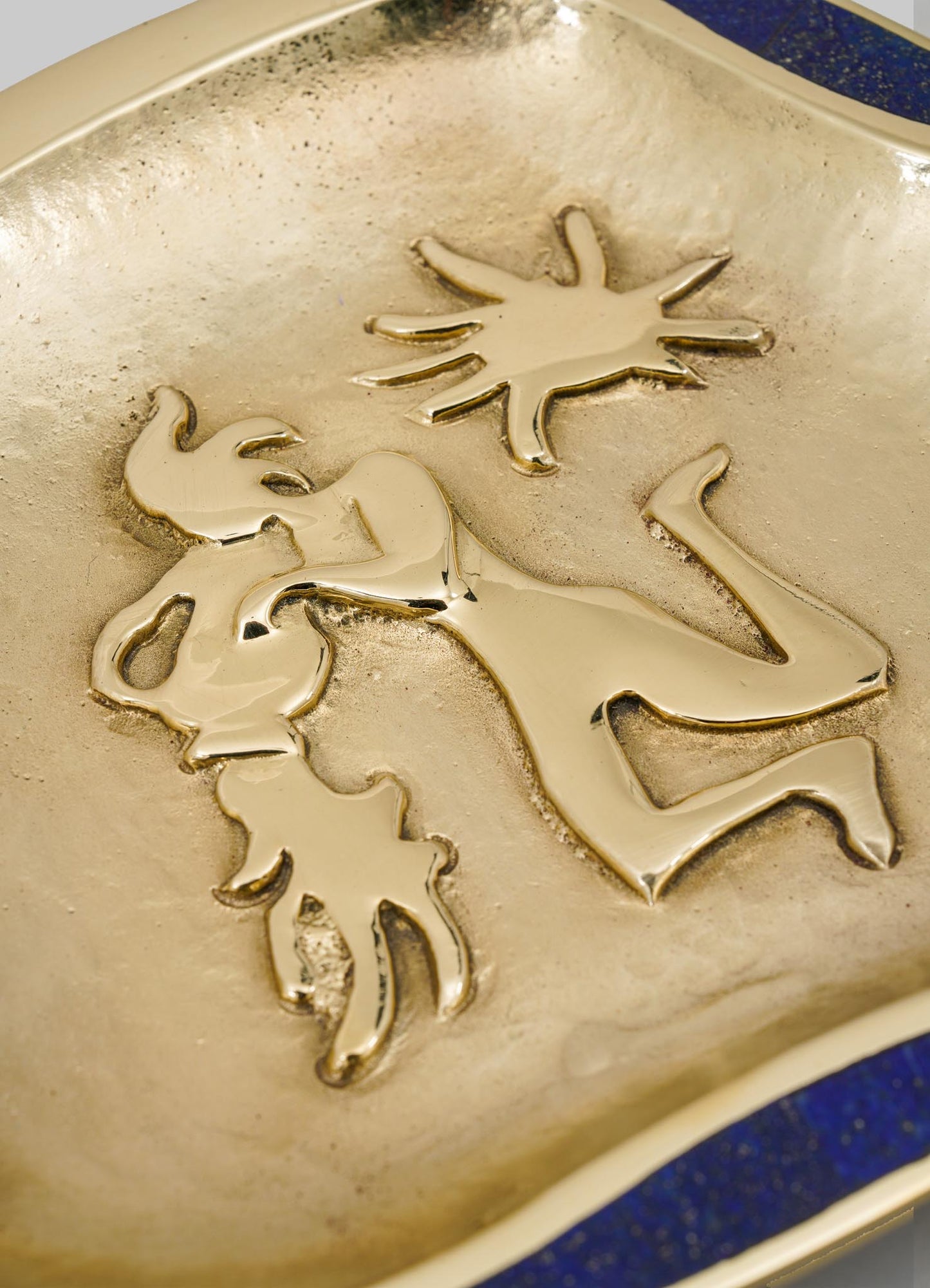 Decorative ceramic dish with a gold-colored finish featuring sculptural figures of a woman and a child, with an additional star motif. The dish has a smooth, glossy surface and a rounded edge with a dark blue accent.