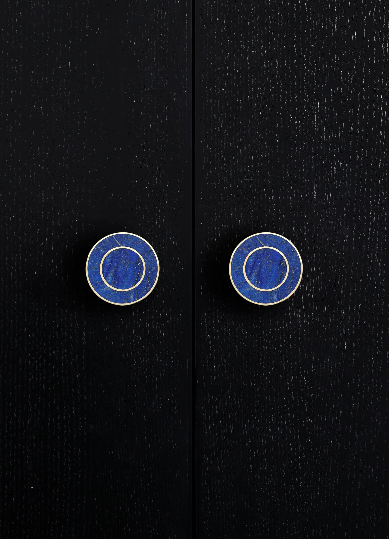 Black wooden doors with visible grain texture, featuring round blue and white ceramic knobs with concentric circle patterns. The style appears modern with a focus on clean lines and contrasting colors.