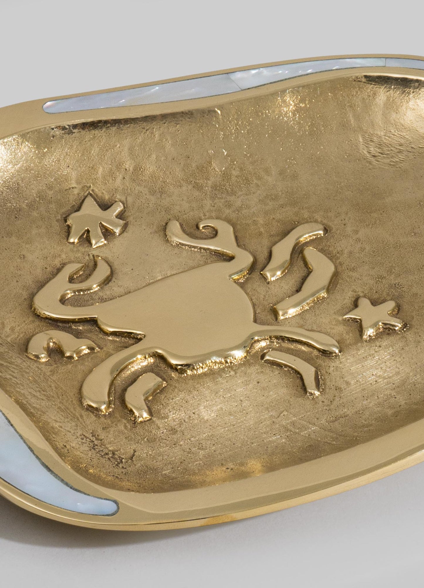 A decorative brass bowl featuring a textured surface with a cut-out design of a cat surrounded by small star motifs, with a polished gold finish. The bowl has an oval shape with smooth edges.