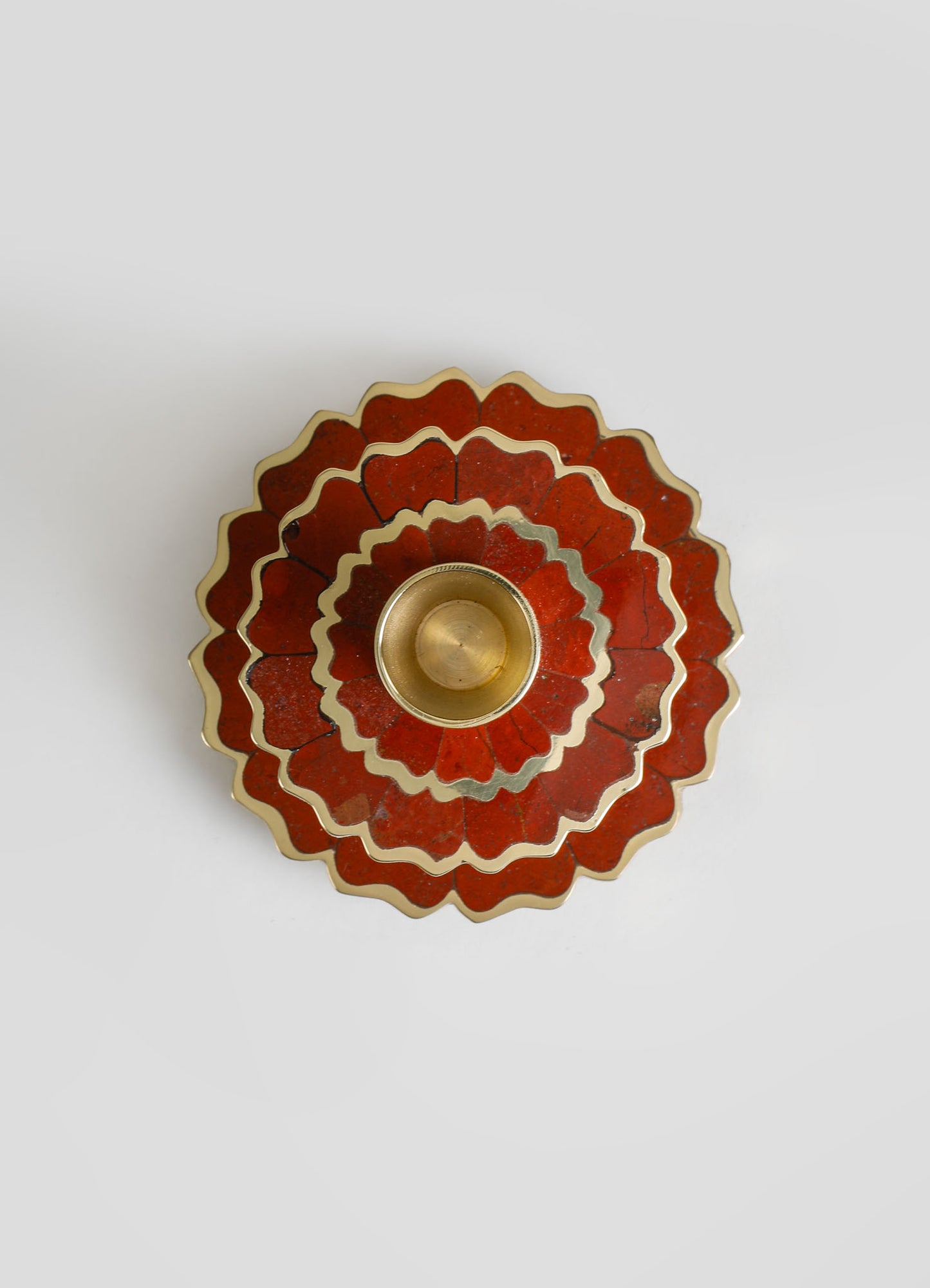 A decorative candle holder with a layered, flower-like design in red and cream tones, featuring scalloped edges and a metallic gold interior.