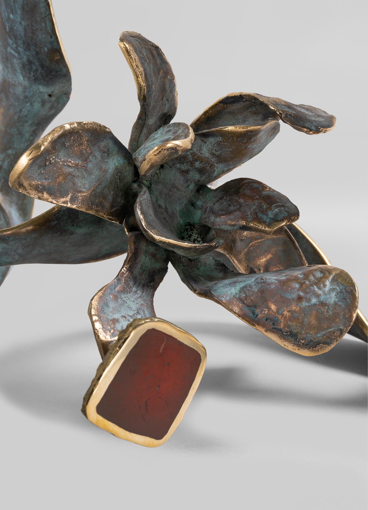 Bronze sculpture with a floral motif, featuring textured, curved petals with metallic gold edges and a patina finish, set against a neutral background.