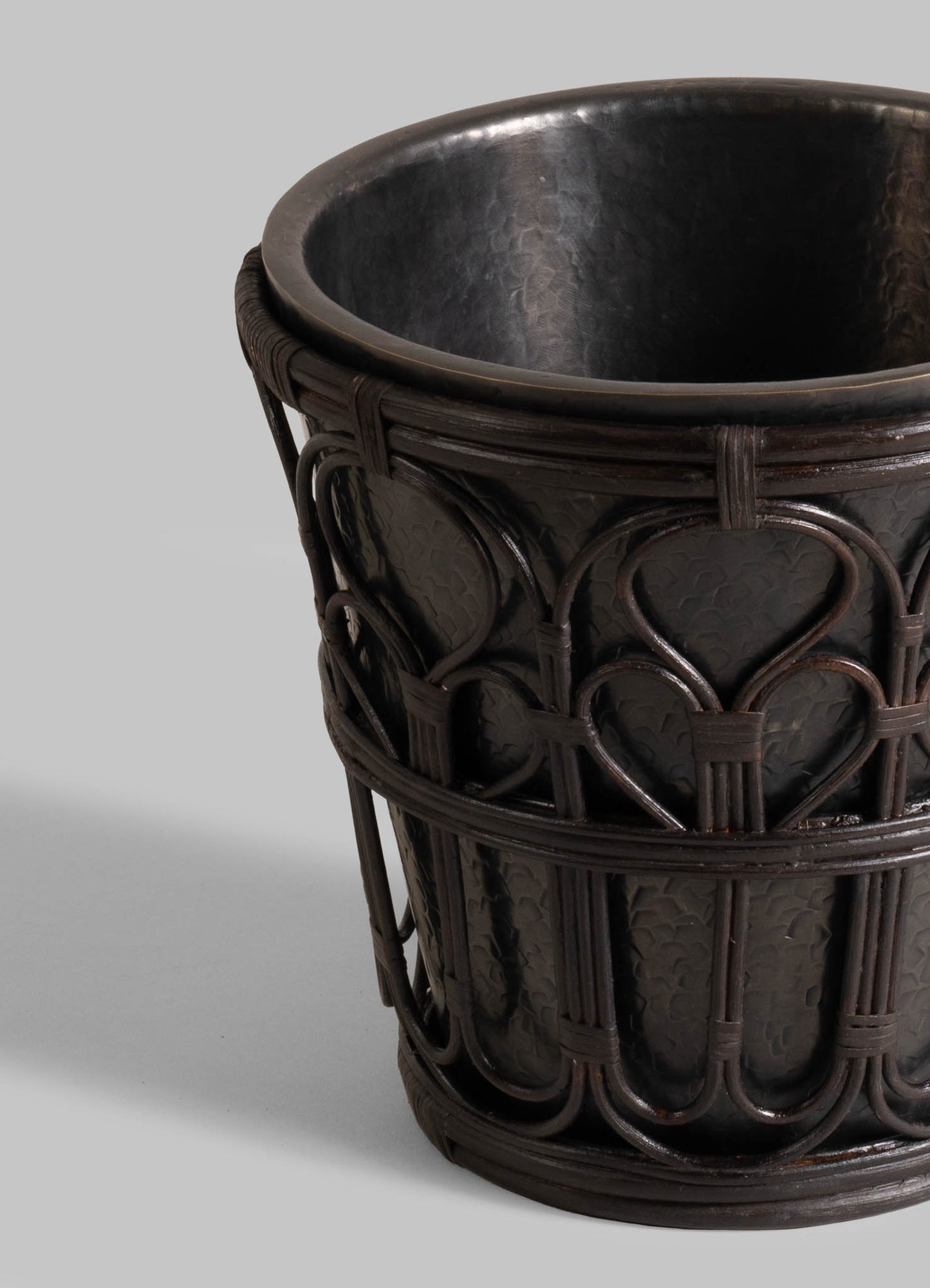 A close-up of the VIYA Manipur Champagne Bucket shows its dark, textured finish and intricate basket-like detailing, inspired by hand-beaten brass. Set against a light gray background, it’s perfect as unique home decor or paired with elegant barware.