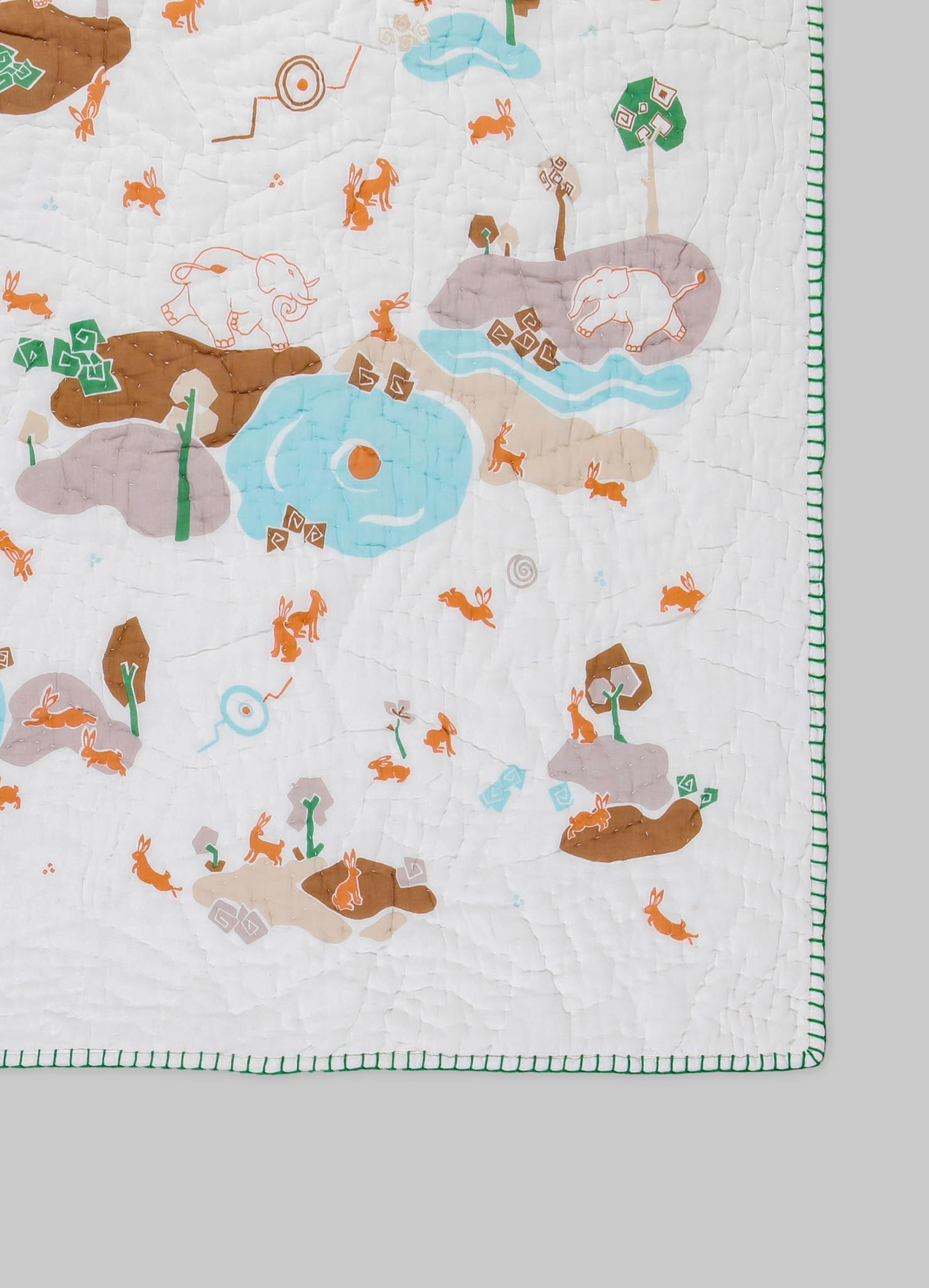 A quilt featuring colorful animal and nature motifs, including rabbits, elephants, and trees, with pastel tones of beige, blue, and brown. The quilt has a stitched pattern and a green striped border.