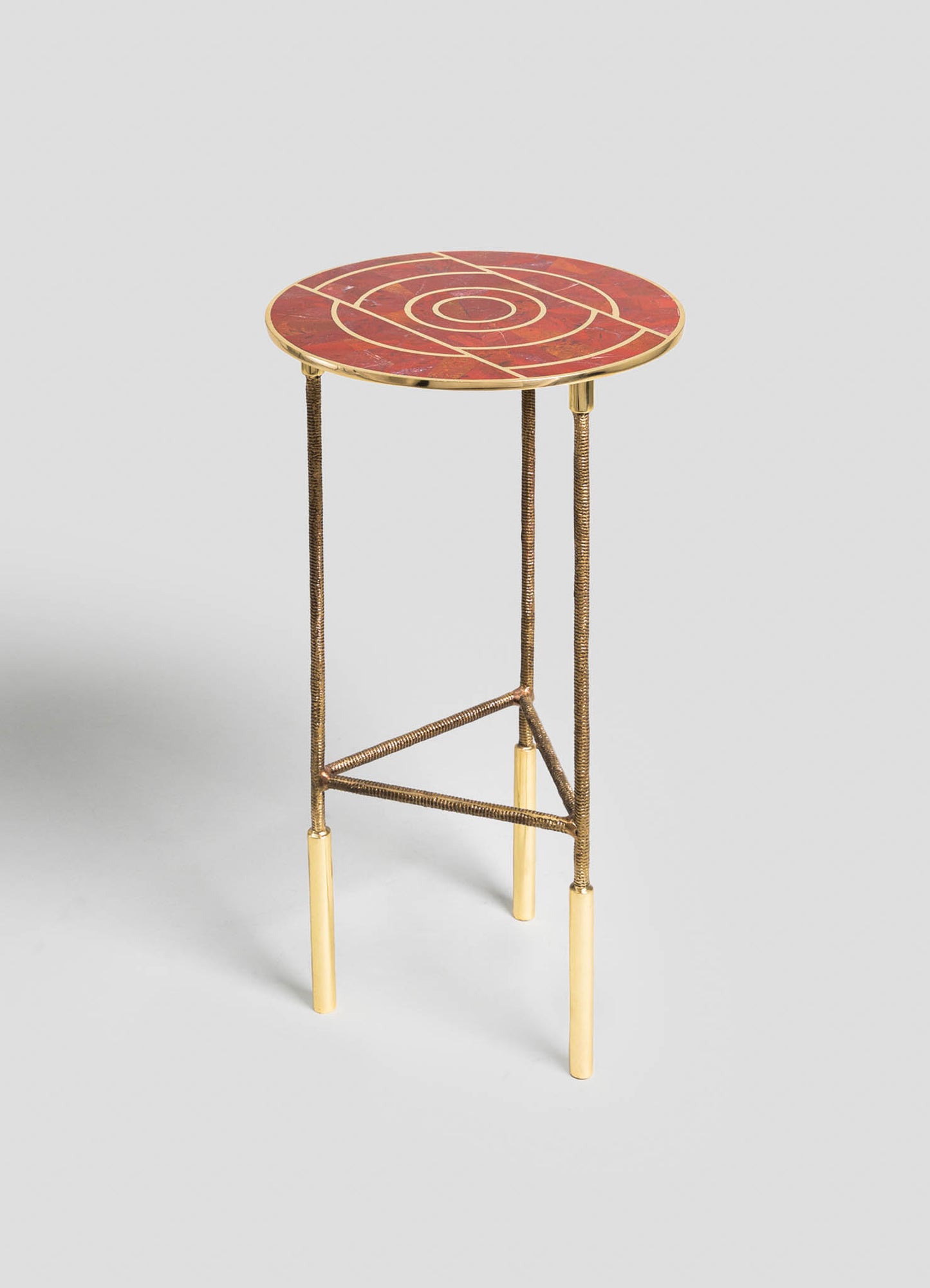 Round side table with a mosaic top featuring geometric patterns in warm red, gold, and beige tones, supported by slender gold and brass-colored legs with beige accents.