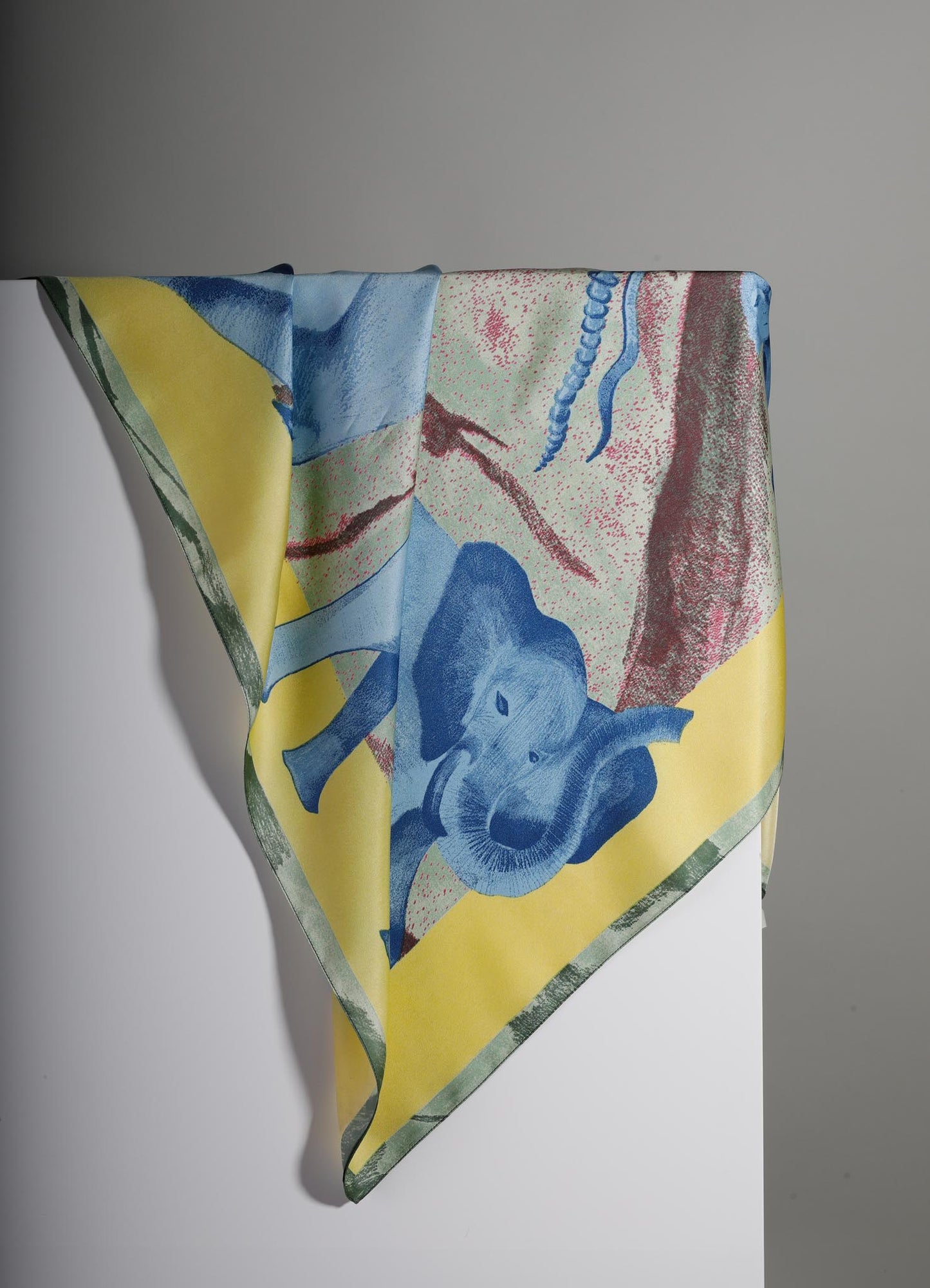 Colorful fabric with an abstract animal and geometric pattern in shades of blue, yellow, green, pink, and red, draped over a white surface. The material appears to be lightweight and printed with a modern, artistic design.