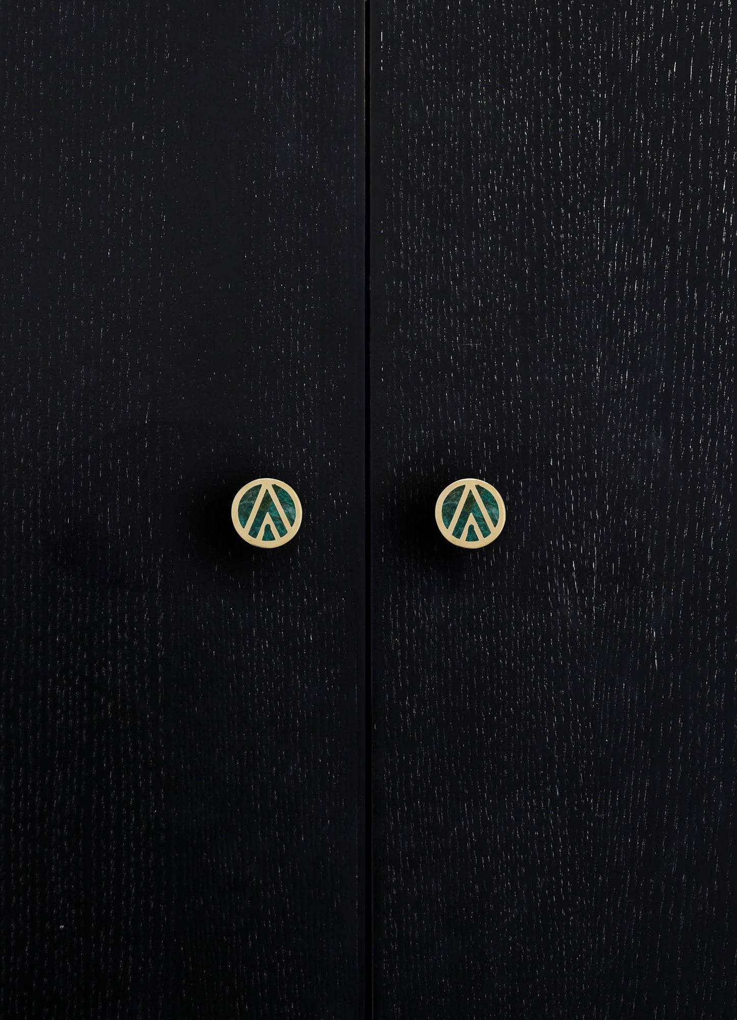 Close-up of black wooden cabinet doors with visible wood grain texture and round metal knobs with geometric cutout designs in a contrasting light finish.