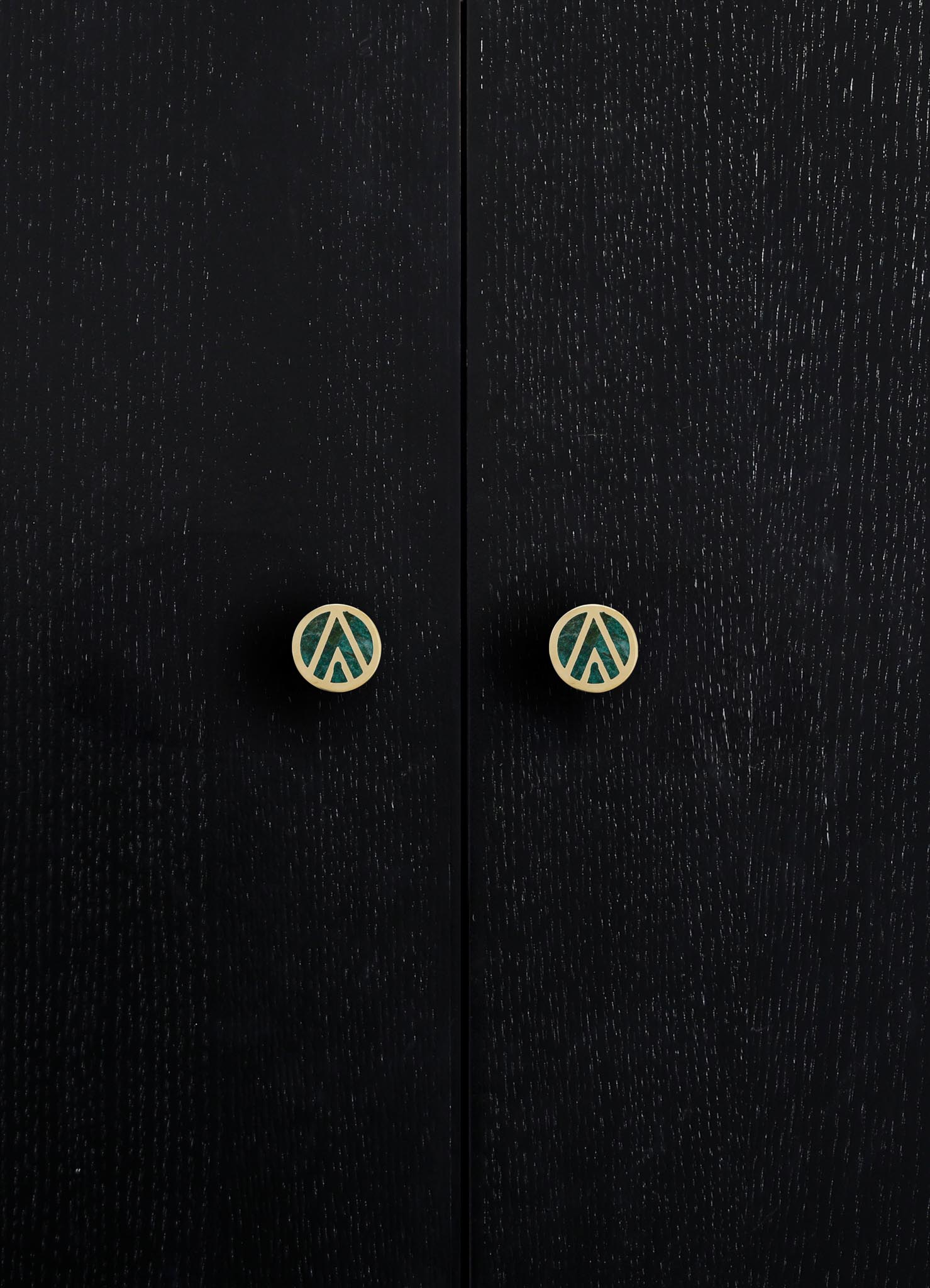 Close-up of black wooden cabinet doors with visible wood grain texture and round metal knobs with geometric cutout designs in a contrasting light finish.