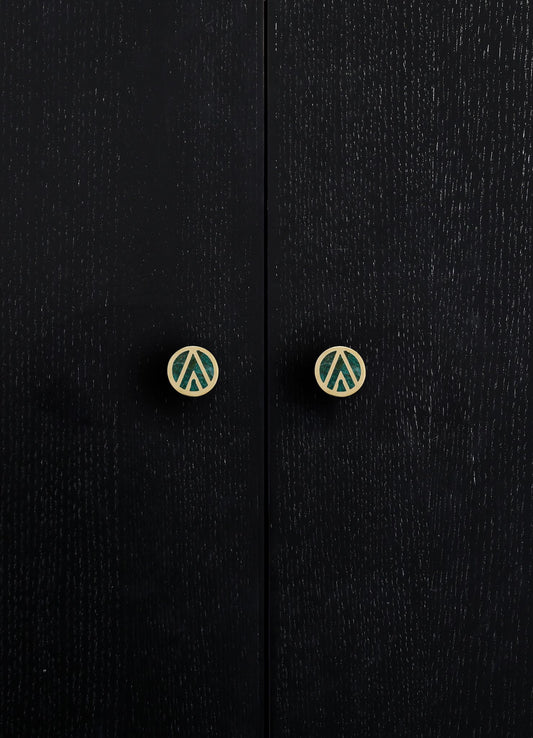 Close-up of black wooden cabinet doors with visible wood grain texture and round metal knobs with geometric cutout designs in a contrasting light finish.