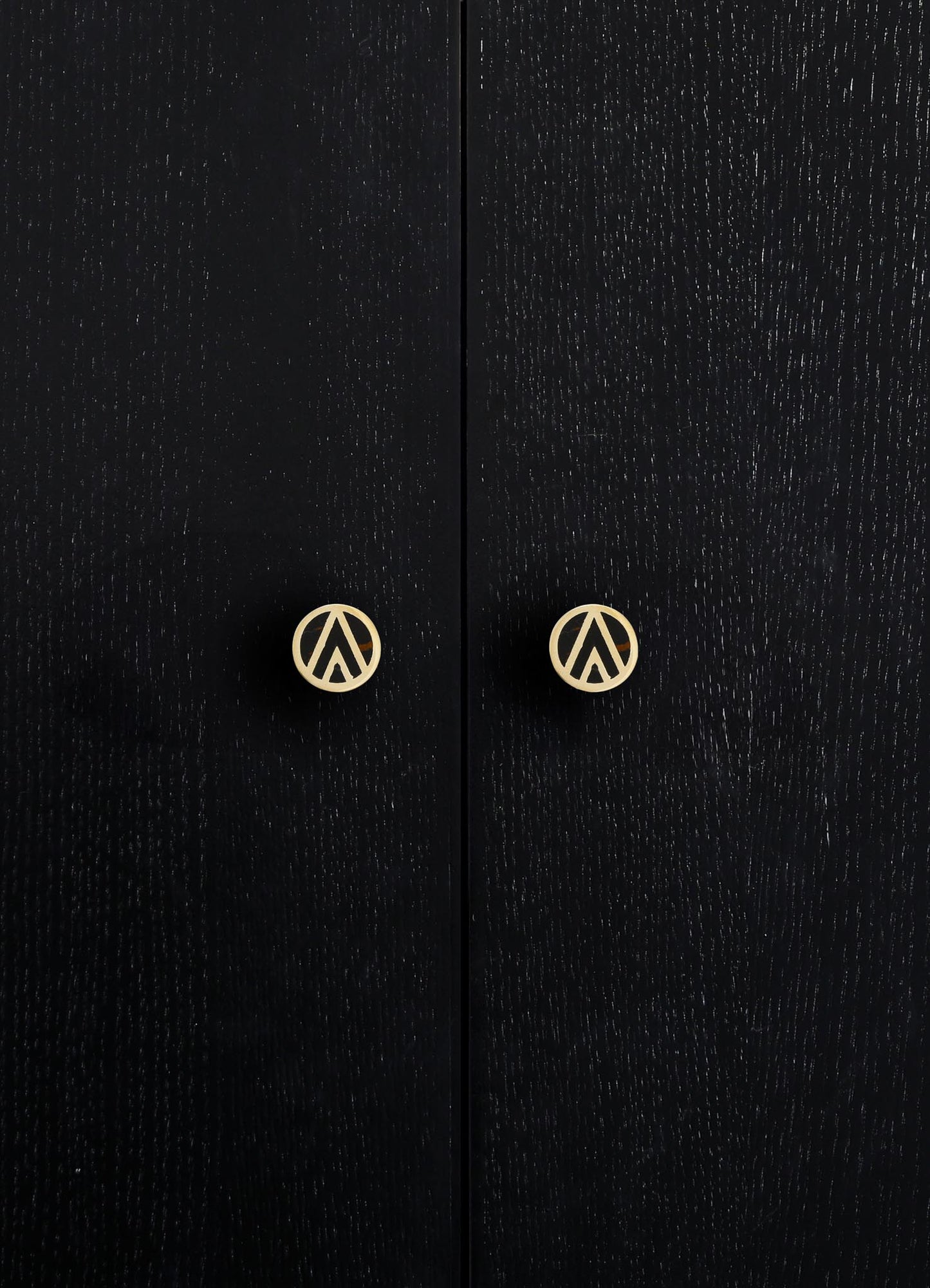 Close-up of black wooden cabinet doors with a textured grain finish, featuring round brass handles with a geometric cutout design.