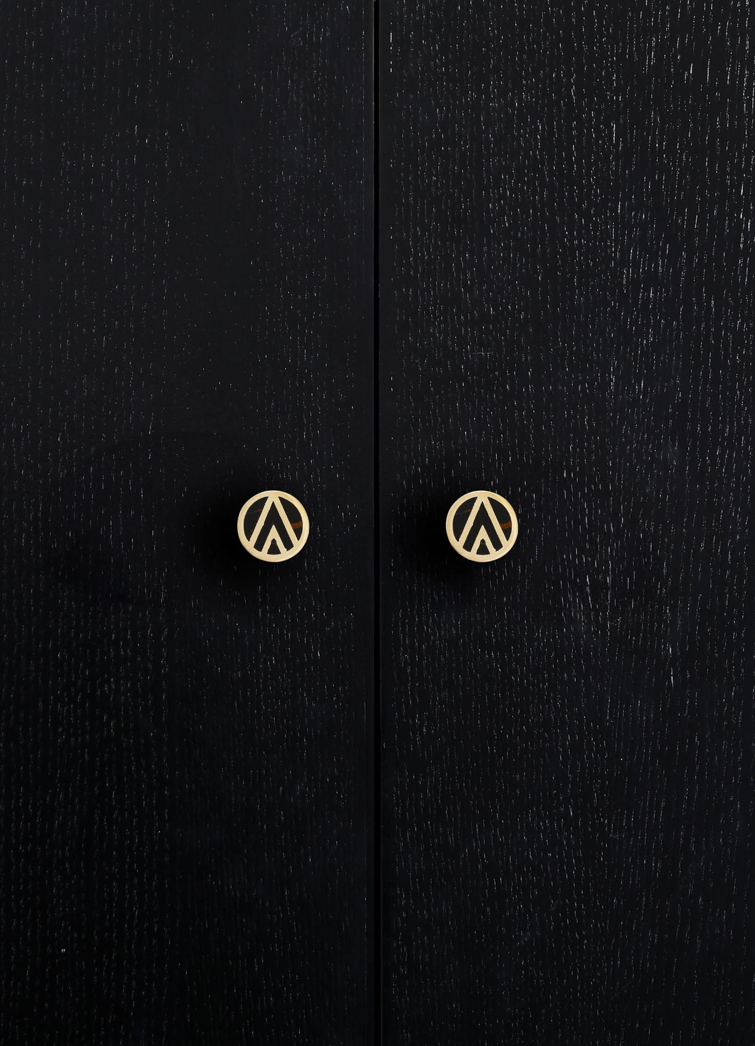 Close-up of black wooden cabinet doors with a textured grain finish, featuring round brass handles with a geometric cutout design.