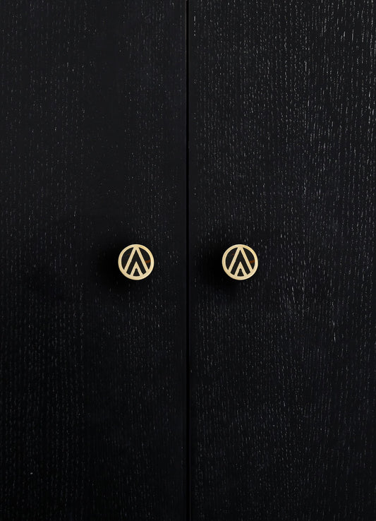 Close-up of black wooden cabinet doors with a textured grain finish, featuring round brass handles with a geometric cutout design.