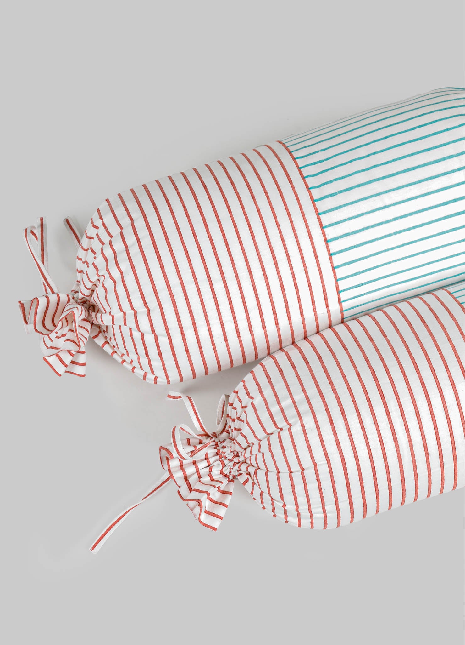 Striped fabric bolsters with red and white, and blue and white lines, featuring tied fabric ties at each end. Made from lightweight textile material with a casual, modern aesthetic.