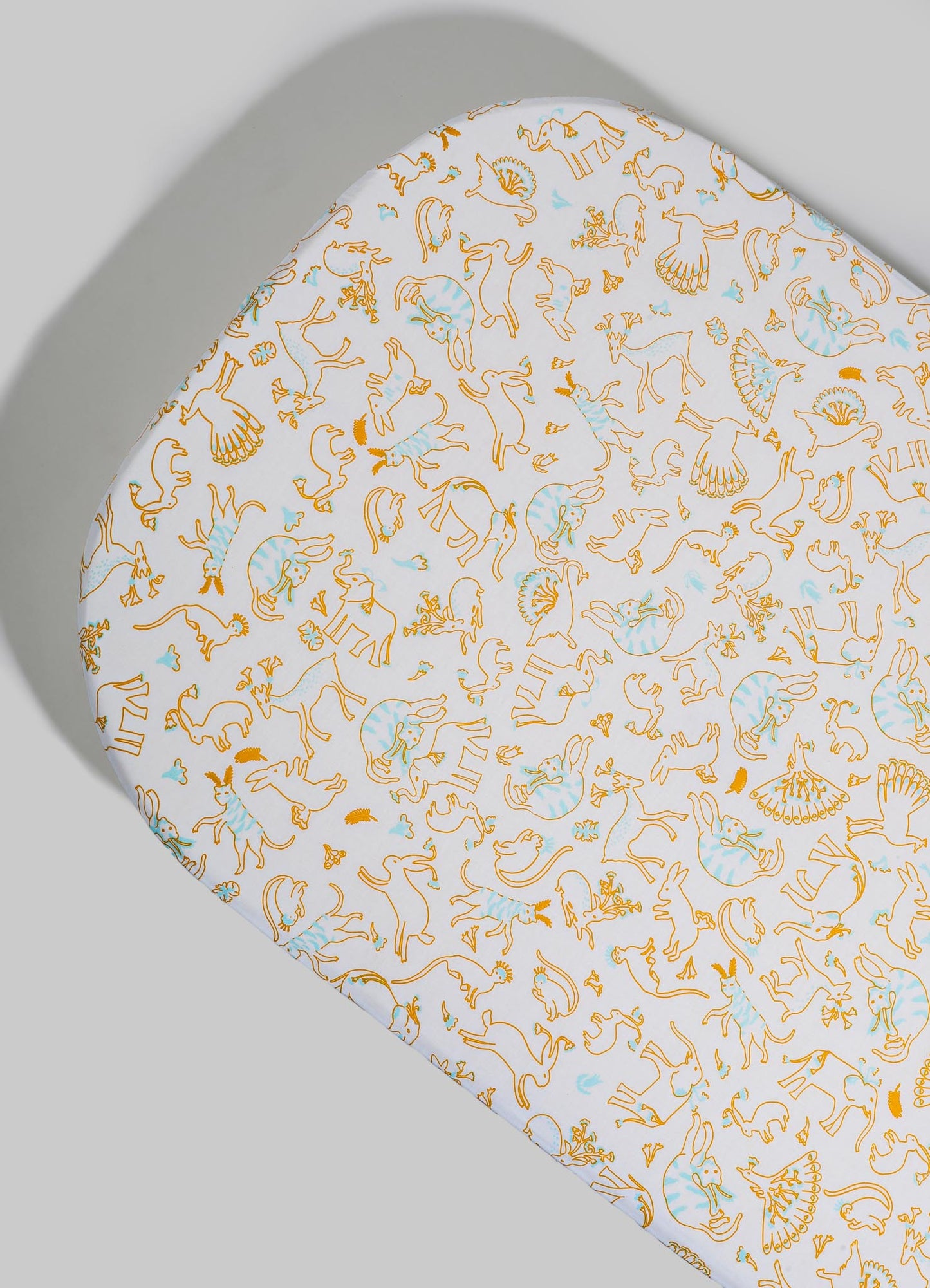 A fabric with a white background featuring a pattern of outlined animals in orange and light blue, including lions, elephants, and birds. The fabric appears smooth and is draped over a surface, highlighting a playful, whimsical design suitable for textiles or home decor.