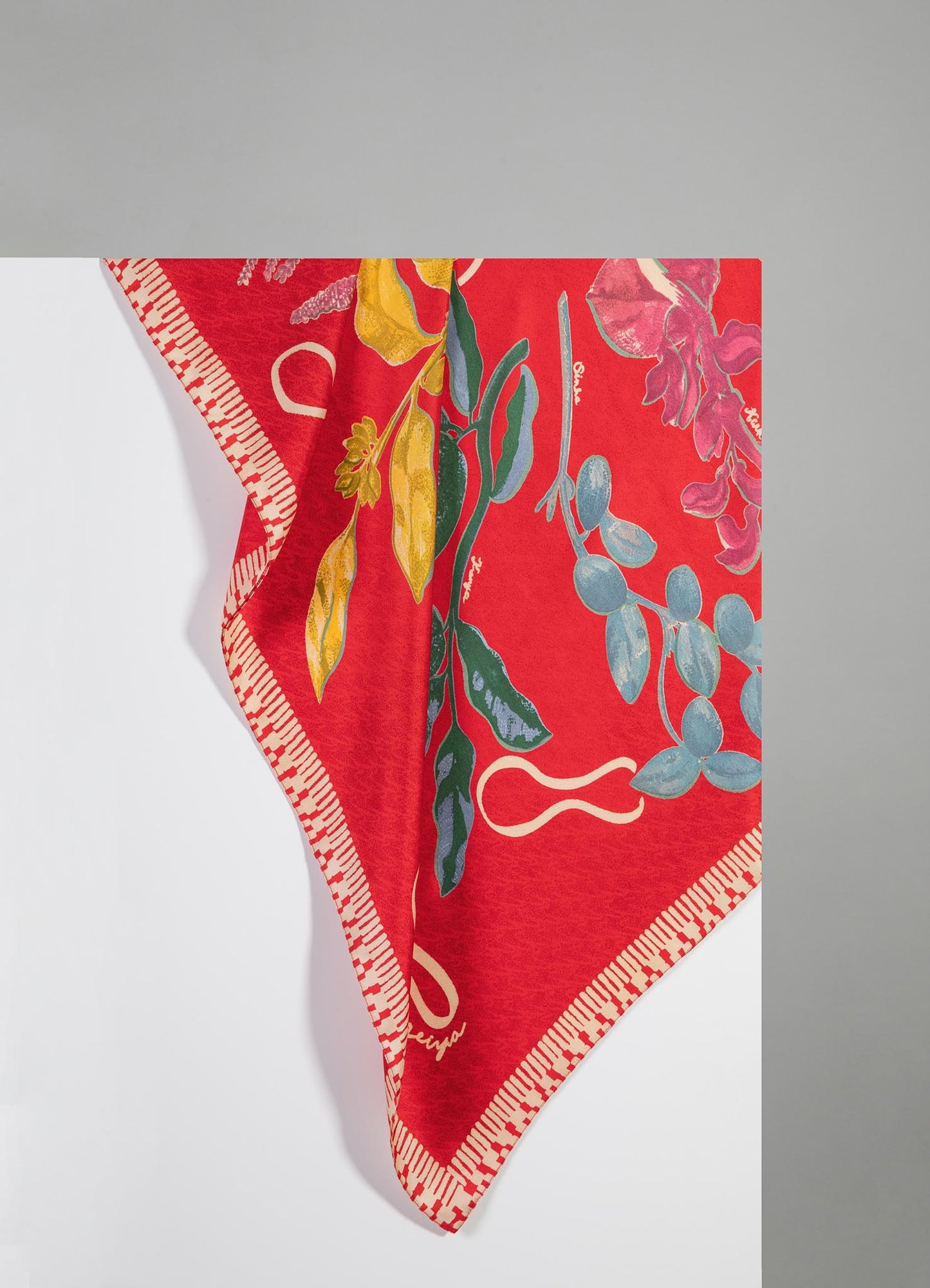 A silk scarf featuring a vibrant floral print with large, colorful flowers and leaves on a red background. The edges are finished with a geometric striped border in red and white.