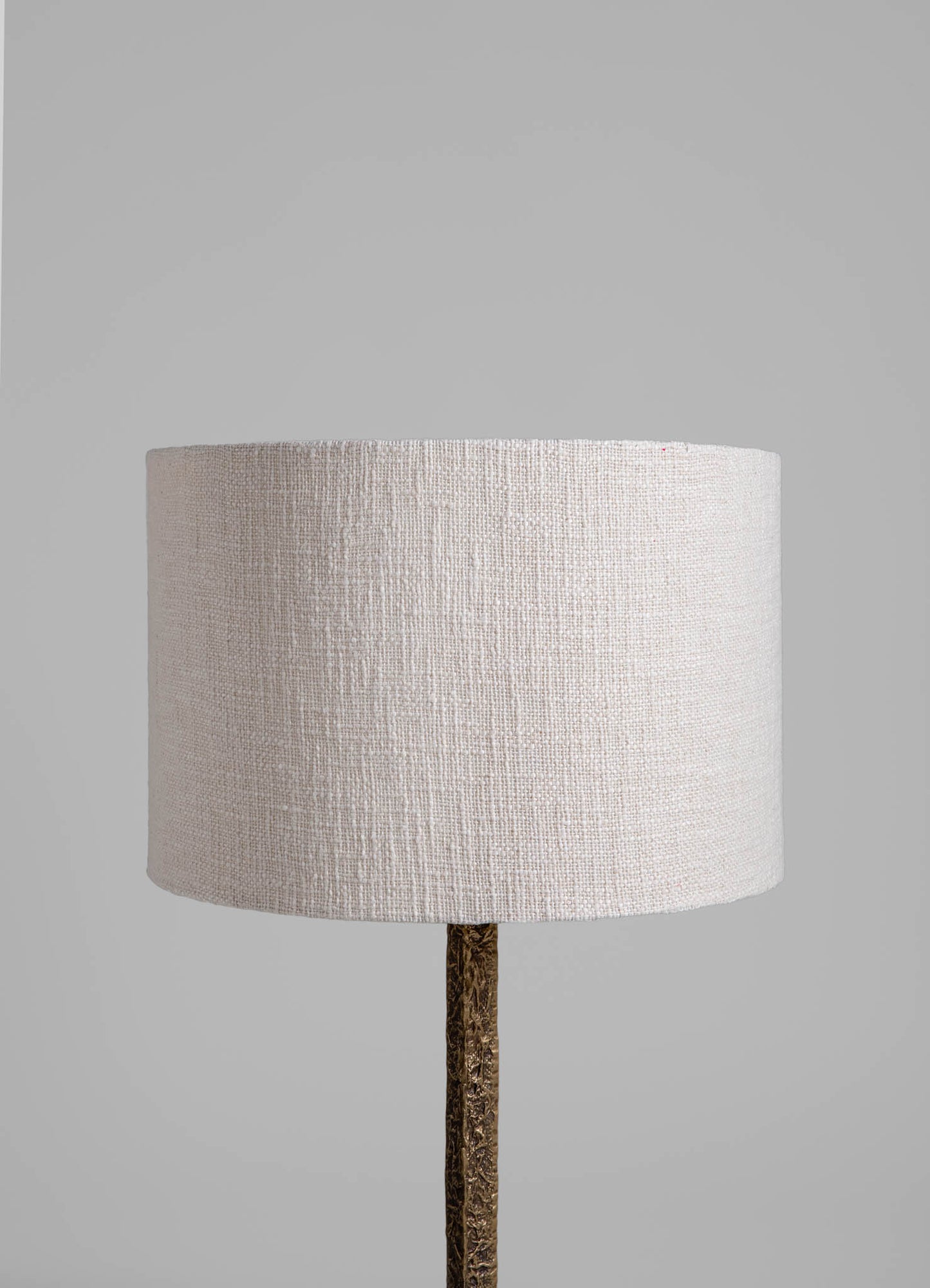 A table lamp with a cylindrical lampshade in beige linen fabric and a textured, metallic gold base, set against a plain background.
