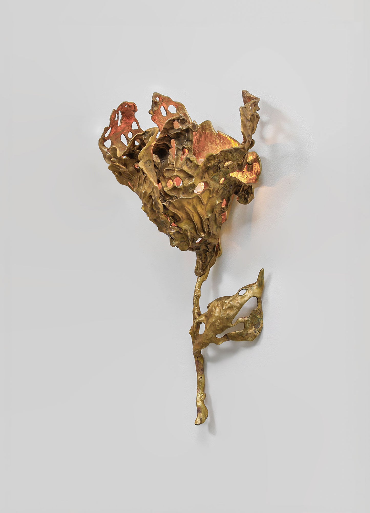 A sculptural wall decoration made of metal with an abstract, organic form resembling a leaf or flower, featuring a textured surface and a combination of gold and copper tones. The piece has a contemporary style with a handcrafted appearance.