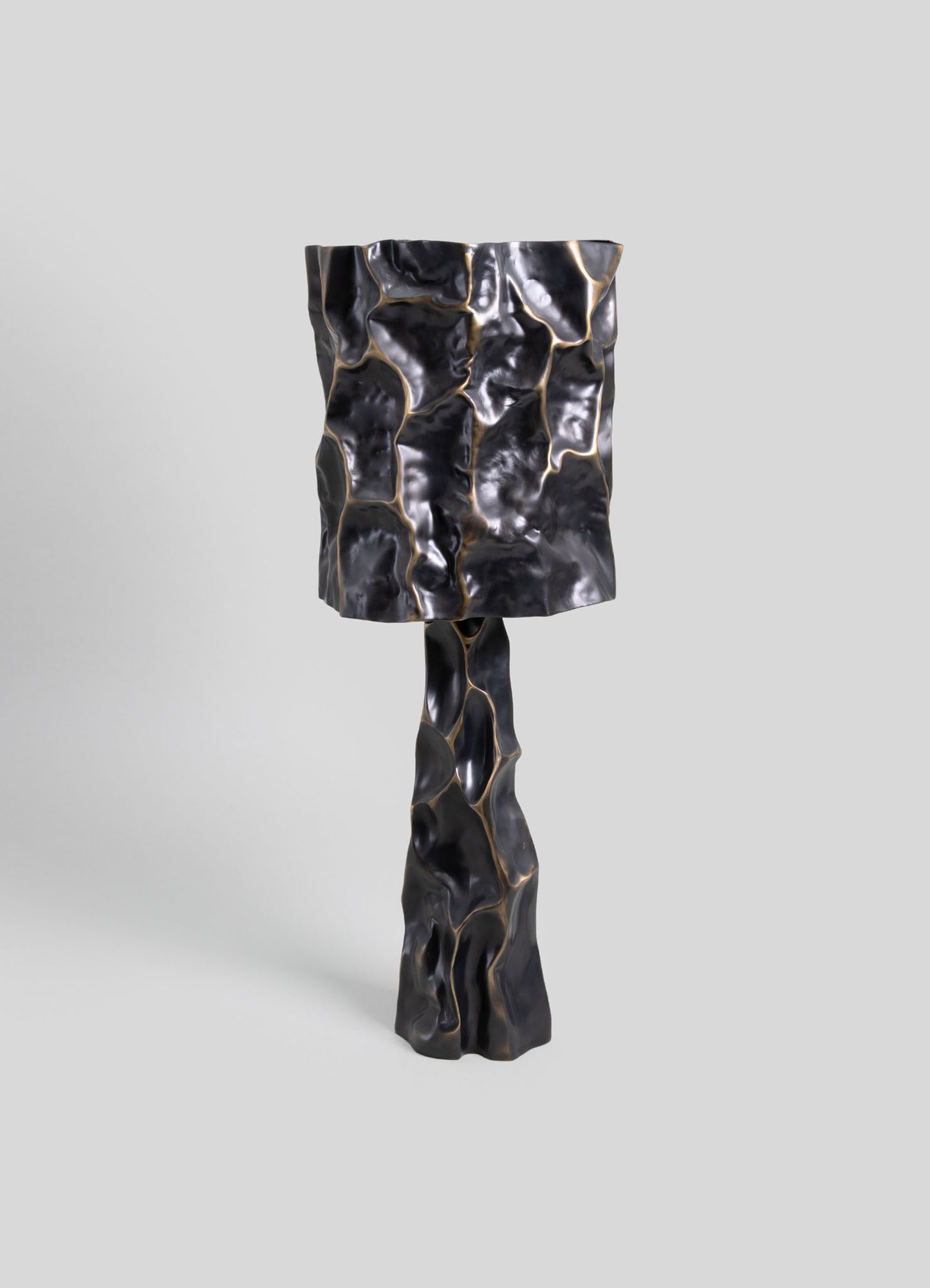 A sculptural floor lamp featuring a textured, crumpled black and gold metallic finish with an abstract, organic form. The design emphasizes a contemporary style with a striking, irregular surface pattern.