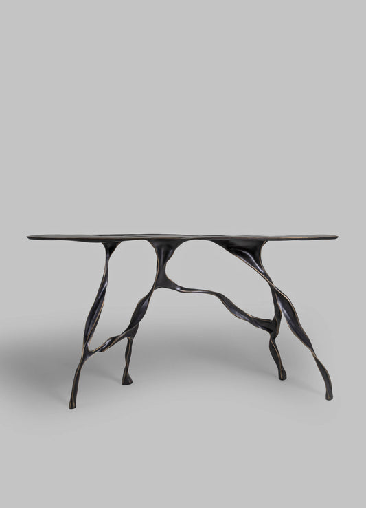A table with a sculptural, organic metal base in a dark finish and a smooth, flat top. The design features flowing, branch-like legs that create a modern, artistic look.