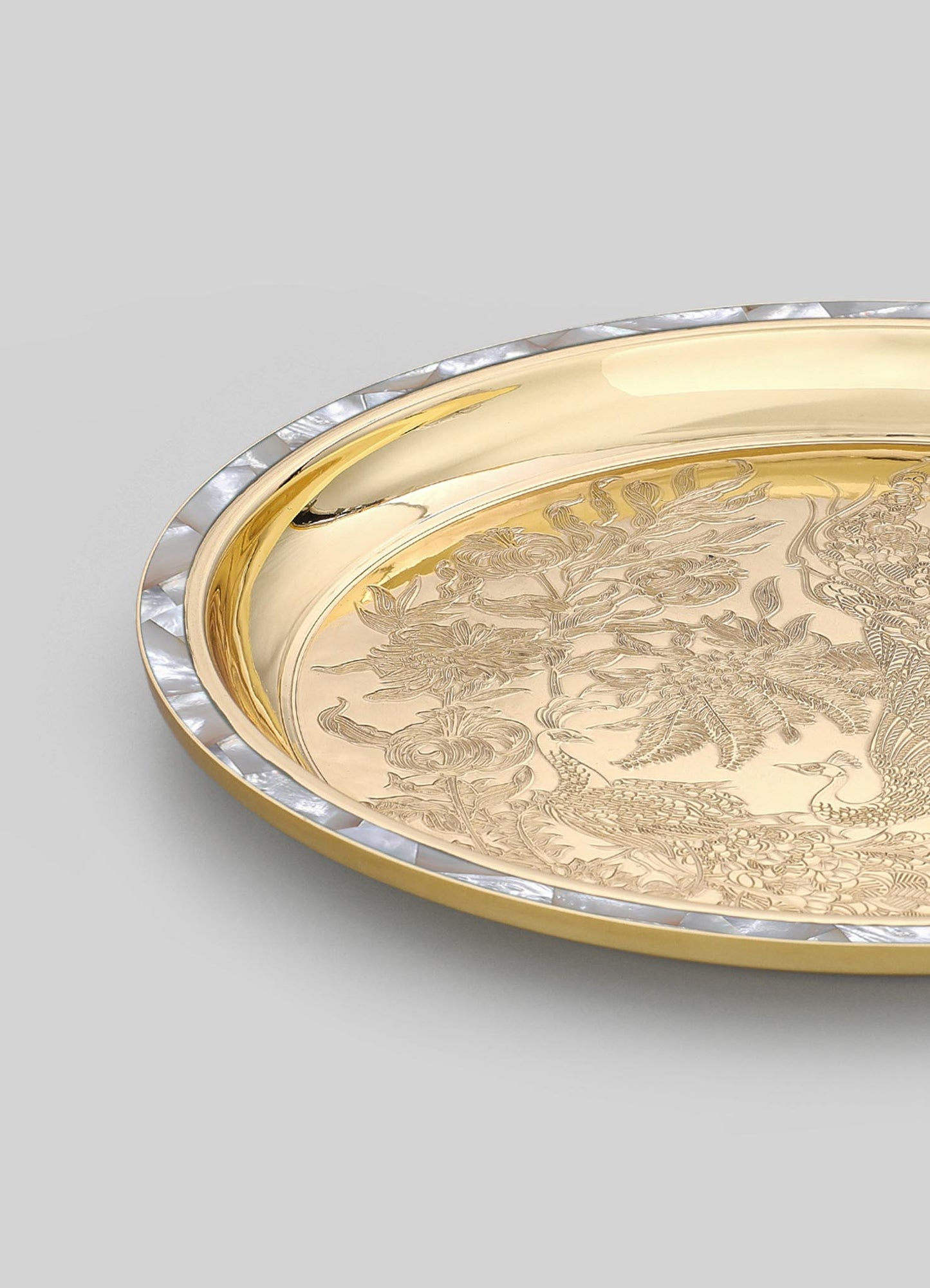 A decorative tray with a gold-toned metal surface engraved with floral and bird motifs, featuring a border of mother-of-pearl inlay on the edge. The tray has a round shape and a polished finish, combining luxury material and intricate design.