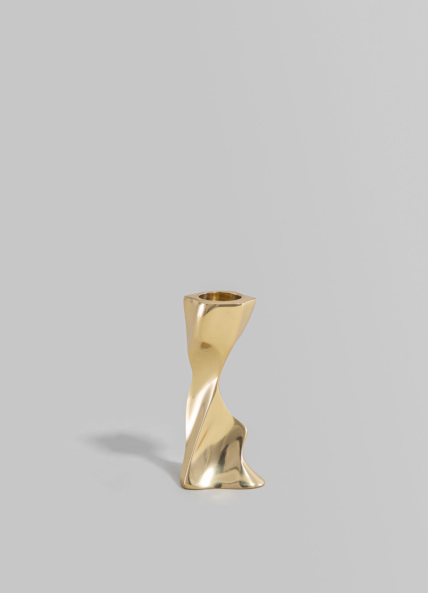 A sculptural brass candle holder with a twisted, organic shape and a polished finish, designed for holding a standard-sized candle.