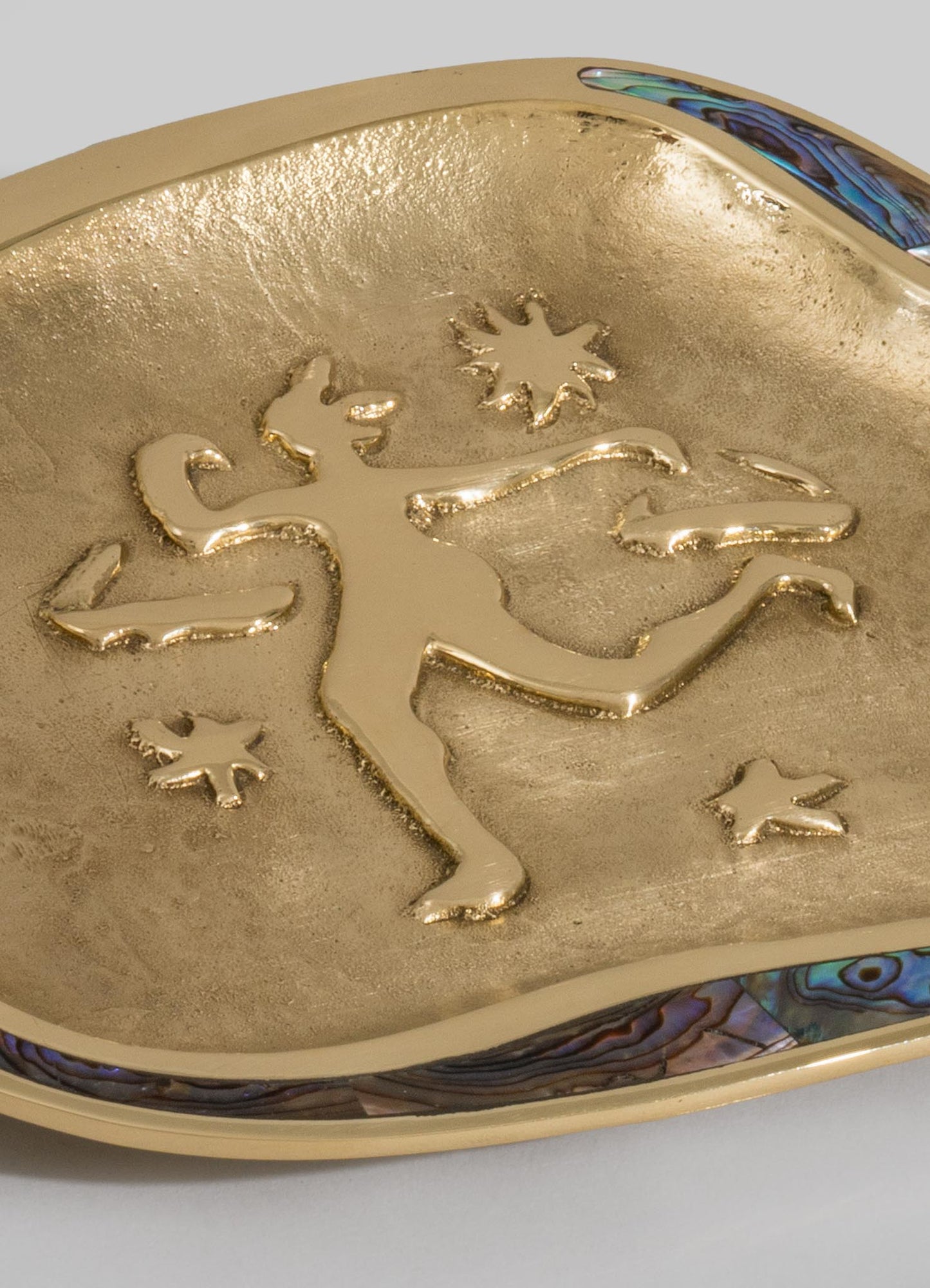 A decorative dish with a metallic gold finish featuring a raised design of a whimsical rainbow, cloud, and star motifs. The dish appears to have a smooth, shiny surface with a colorful abalone shell trim along the edge.