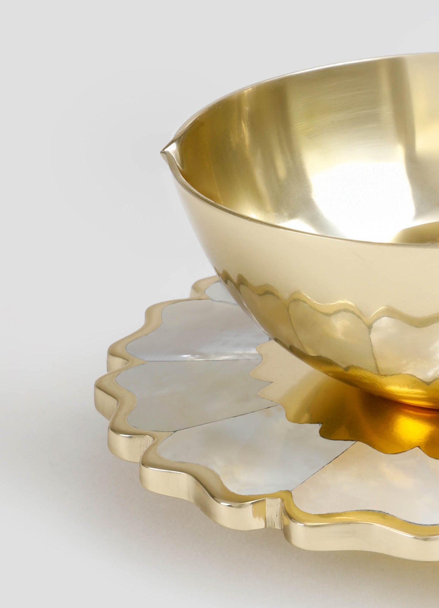 A gold-colored metal bowl with a smooth, reflective surface, paired with a scalloped-edged metal tray in a matching finish, featuring a mix of gold and silver tones. The design is contemporary with a luxurious, minimalist aesthetic.