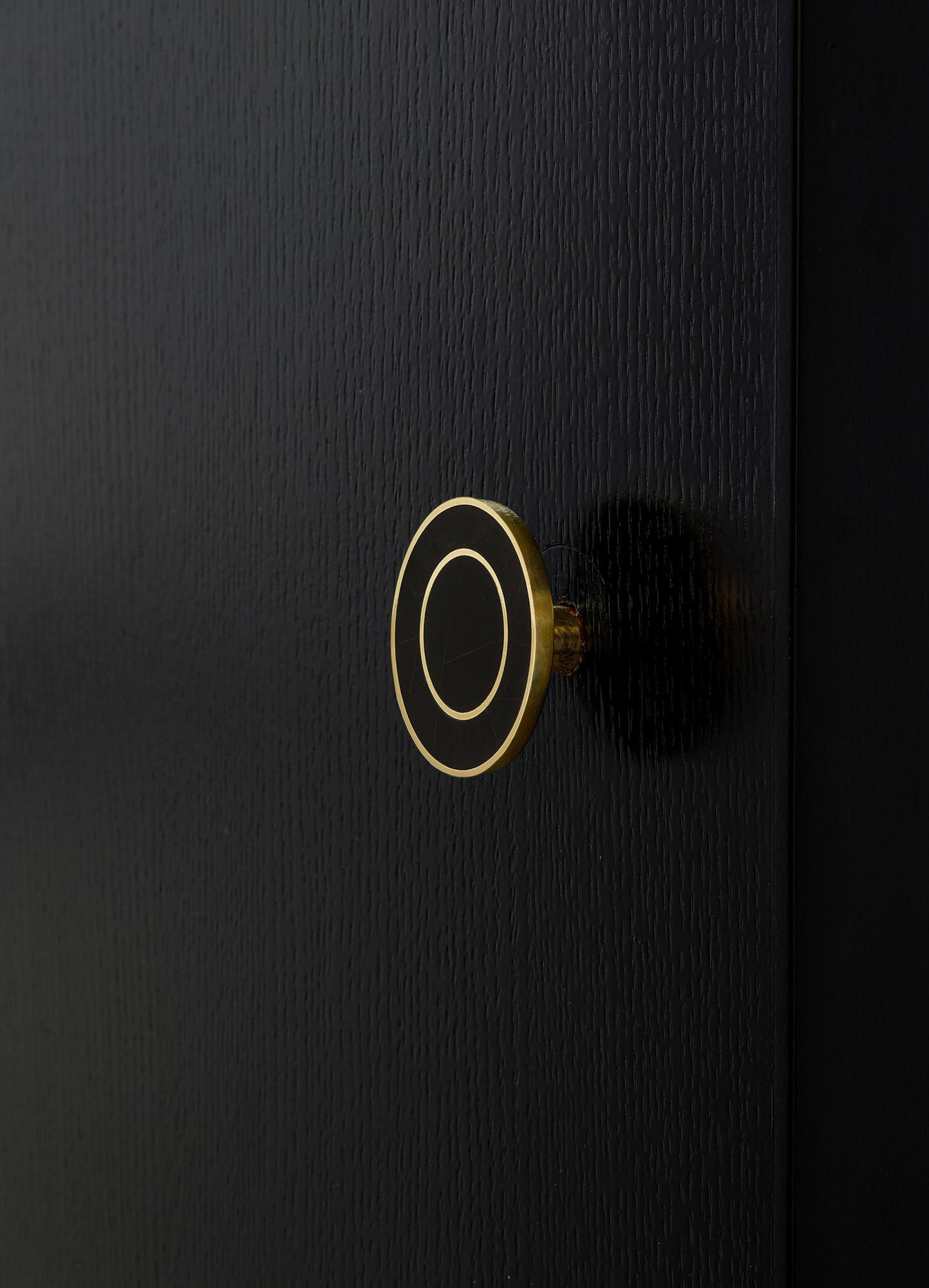 A close-up of a black textured door with a round, modern door handle featuring a black and gold circular design. The handle has a sleek, minimalistic style with a smooth finish.