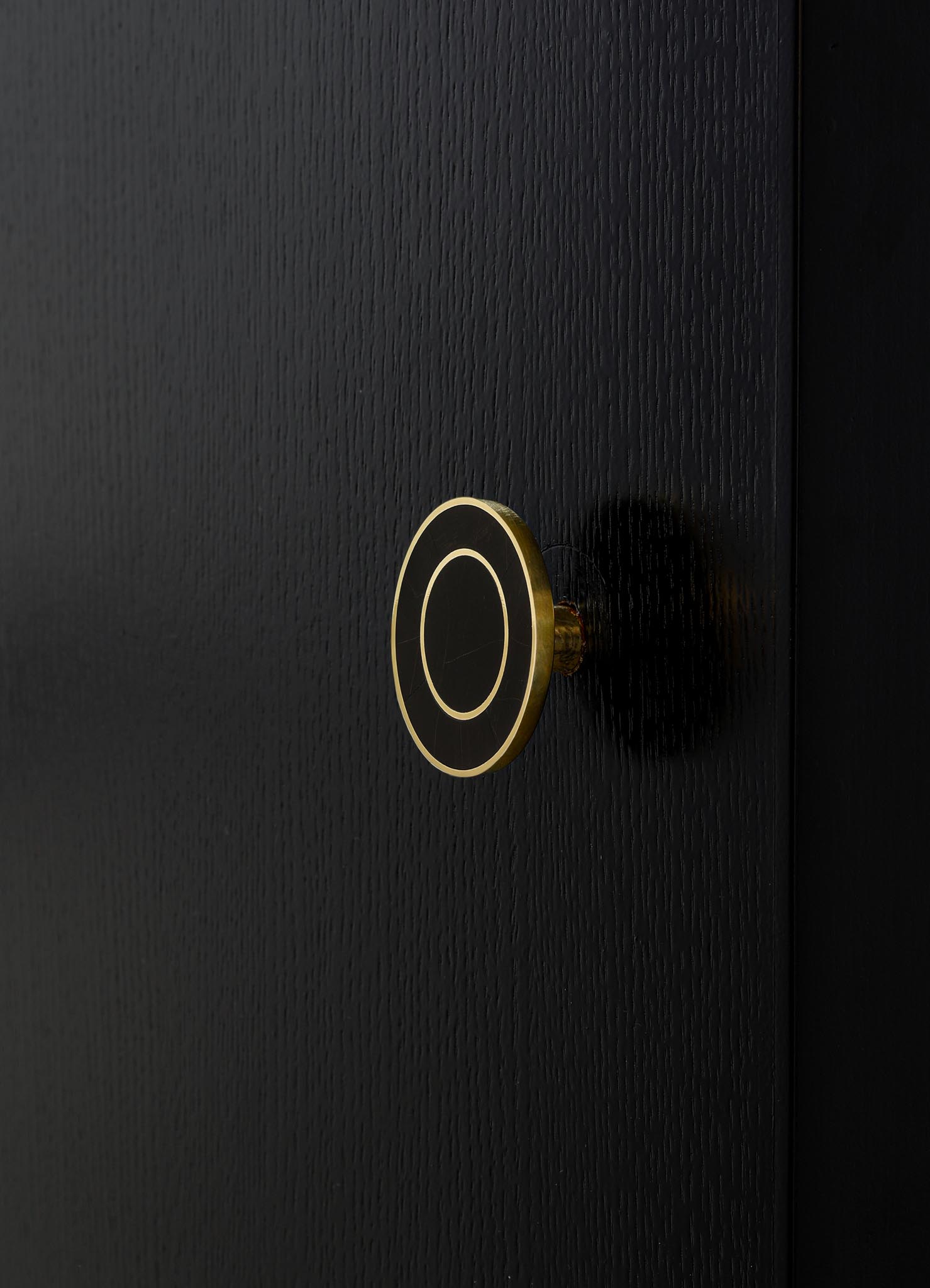 A close-up of a black textured door with a round, modern door handle featuring a black and gold circular design. The handle has a sleek, minimalistic style with a smooth finish.