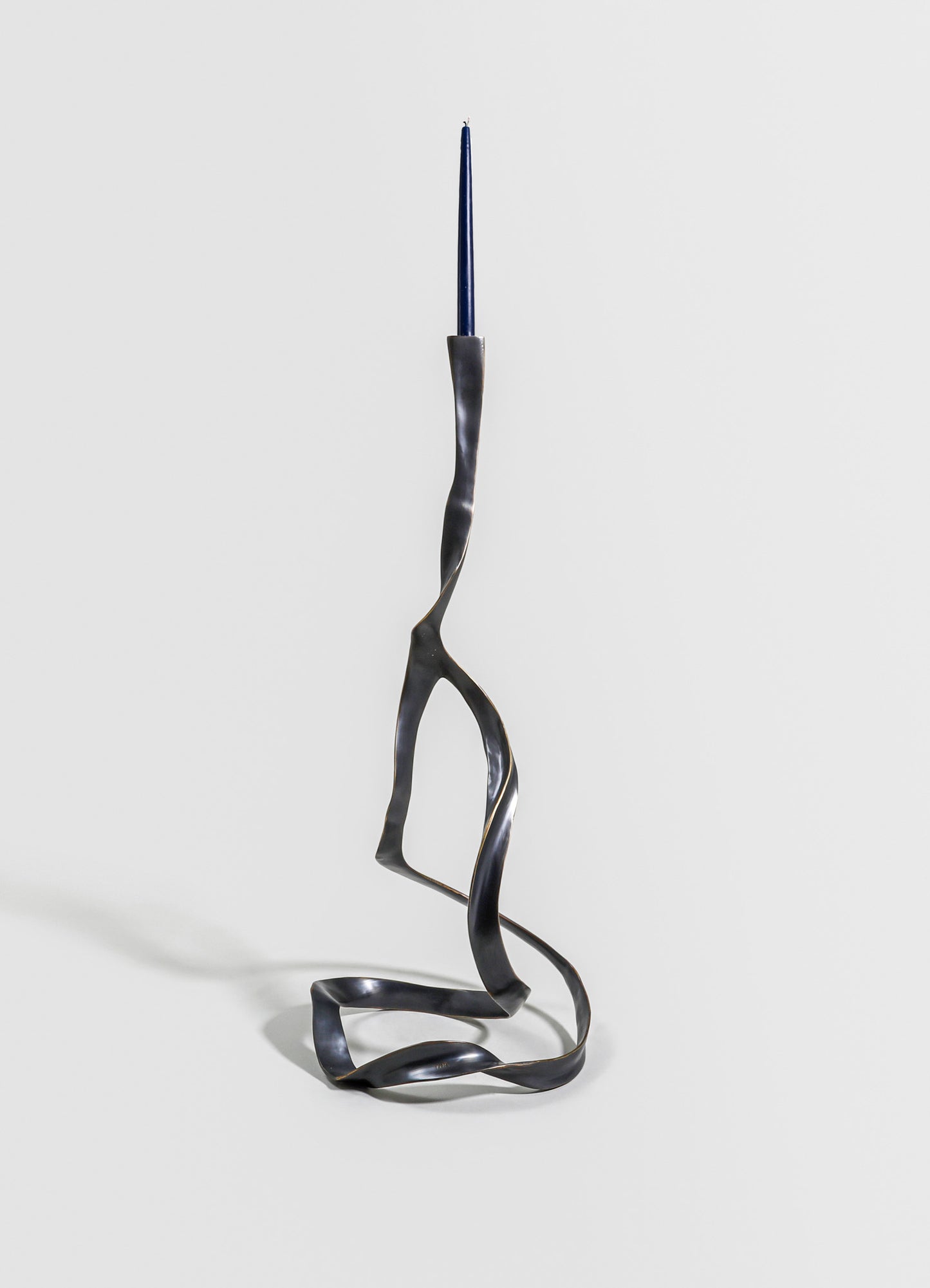 A sculptural candle holder made of twisted, black metal with an abstract, artistic design. It features a tall, slim blue taper candle at the top and has a contemporary, minimalist style.