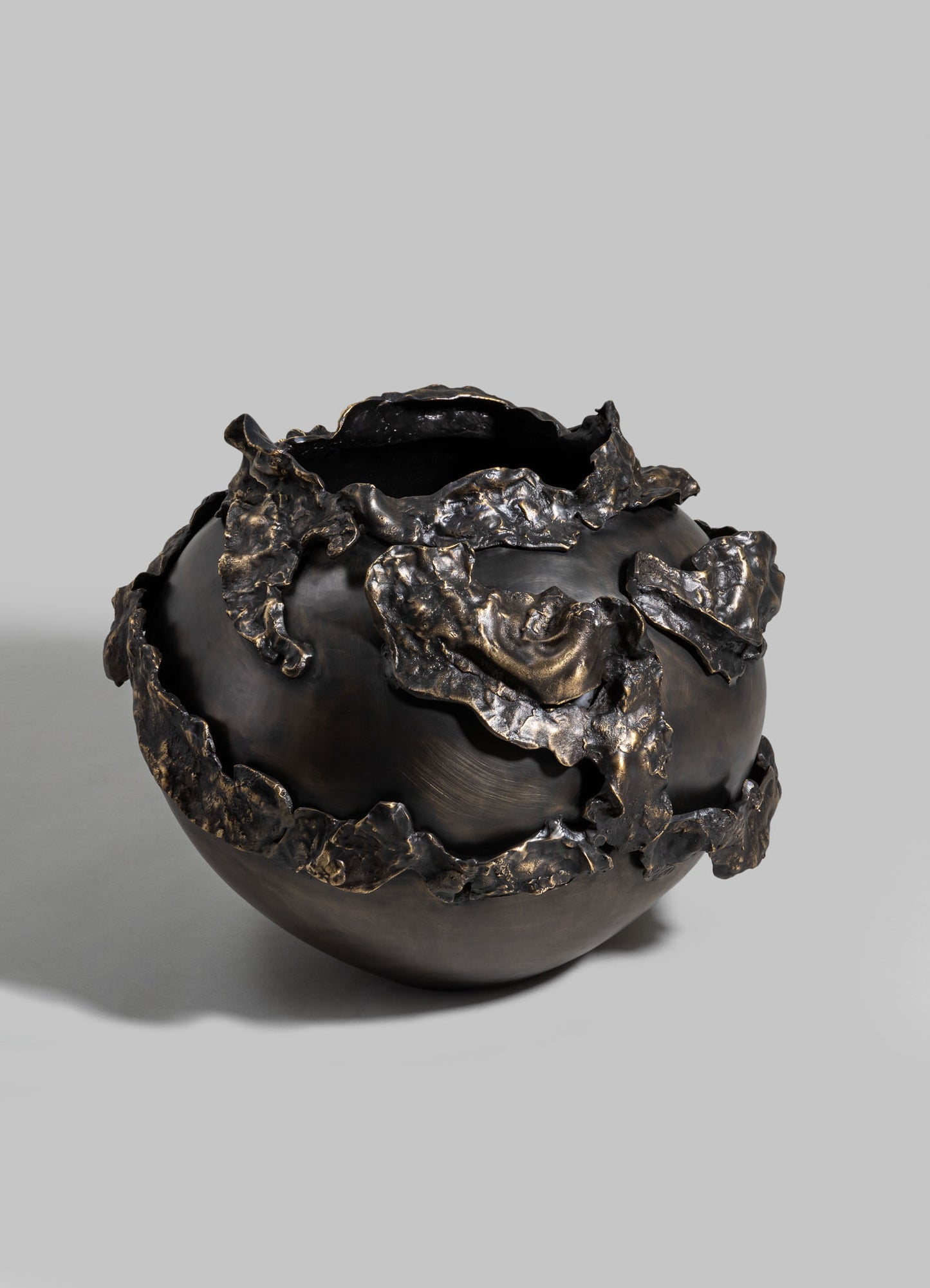 A black ceramic vase with irregular, textured metallic gold accents resembling molten or crumpled metal, showcasing an abstract and contemporary design.