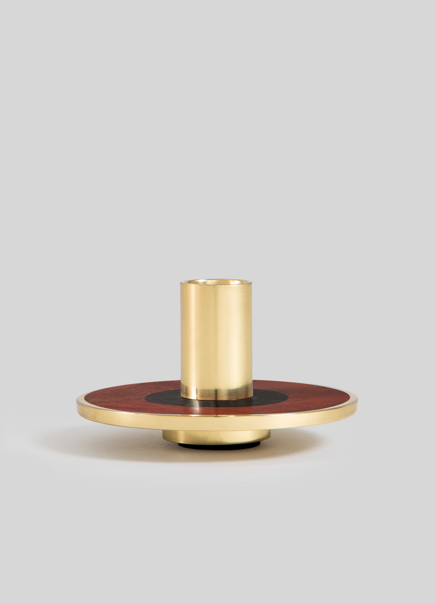 A decorative candle holder with a cylindrical brass insert mounted on a round wooden base featuring a dark circular motif and a brass rim, set against a plain background.