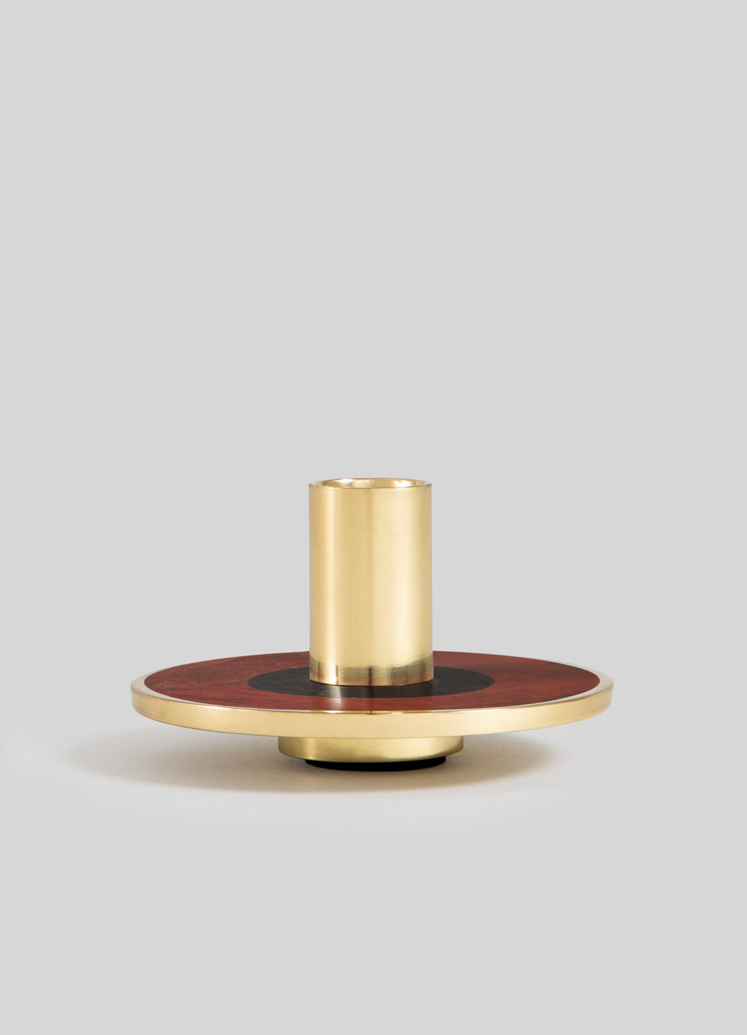 A decorative candle holder with a cylindrical brass insert mounted on a round wooden base featuring a dark circular motif and a brass rim, set against a plain background.