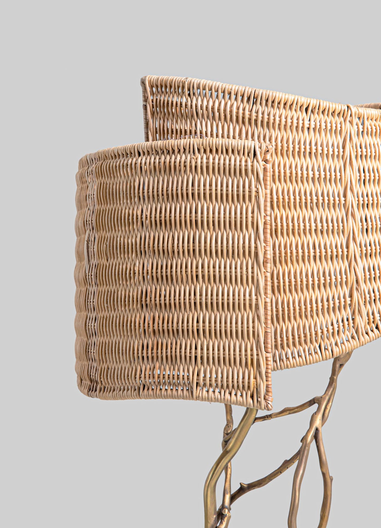 Woven rattan basket with a natural finish, featuring a rectangular shape and intricate interlaced pattern. The basket is supported by curved, branch-like metal legs with a brushed gold finish, creating a rustic and contemporary contrast.