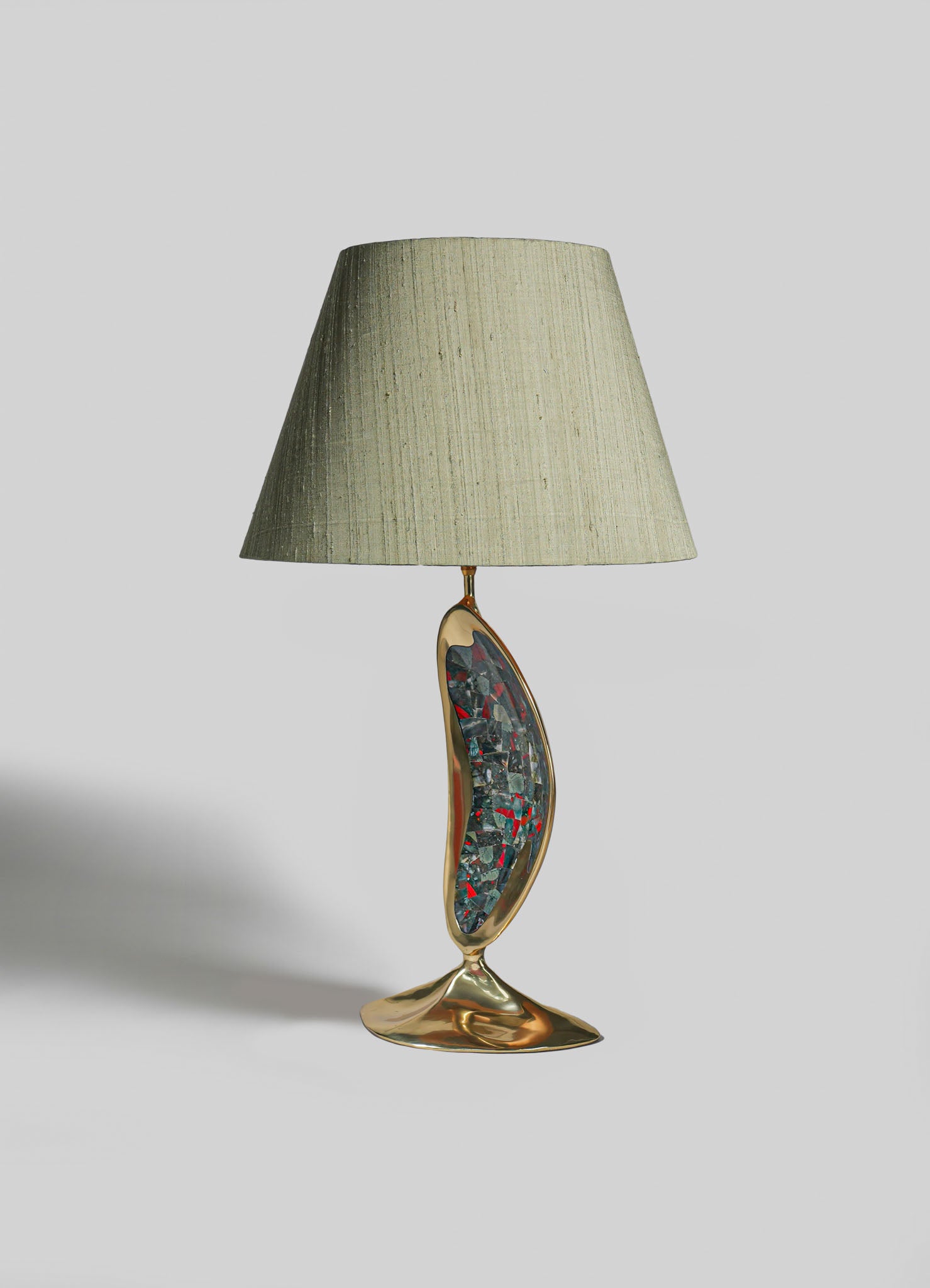 Table lamp with a beige fabric shade and a sculptural ceramic base featuring a colorful mosaic pattern, mounted on a metallic gold stand.