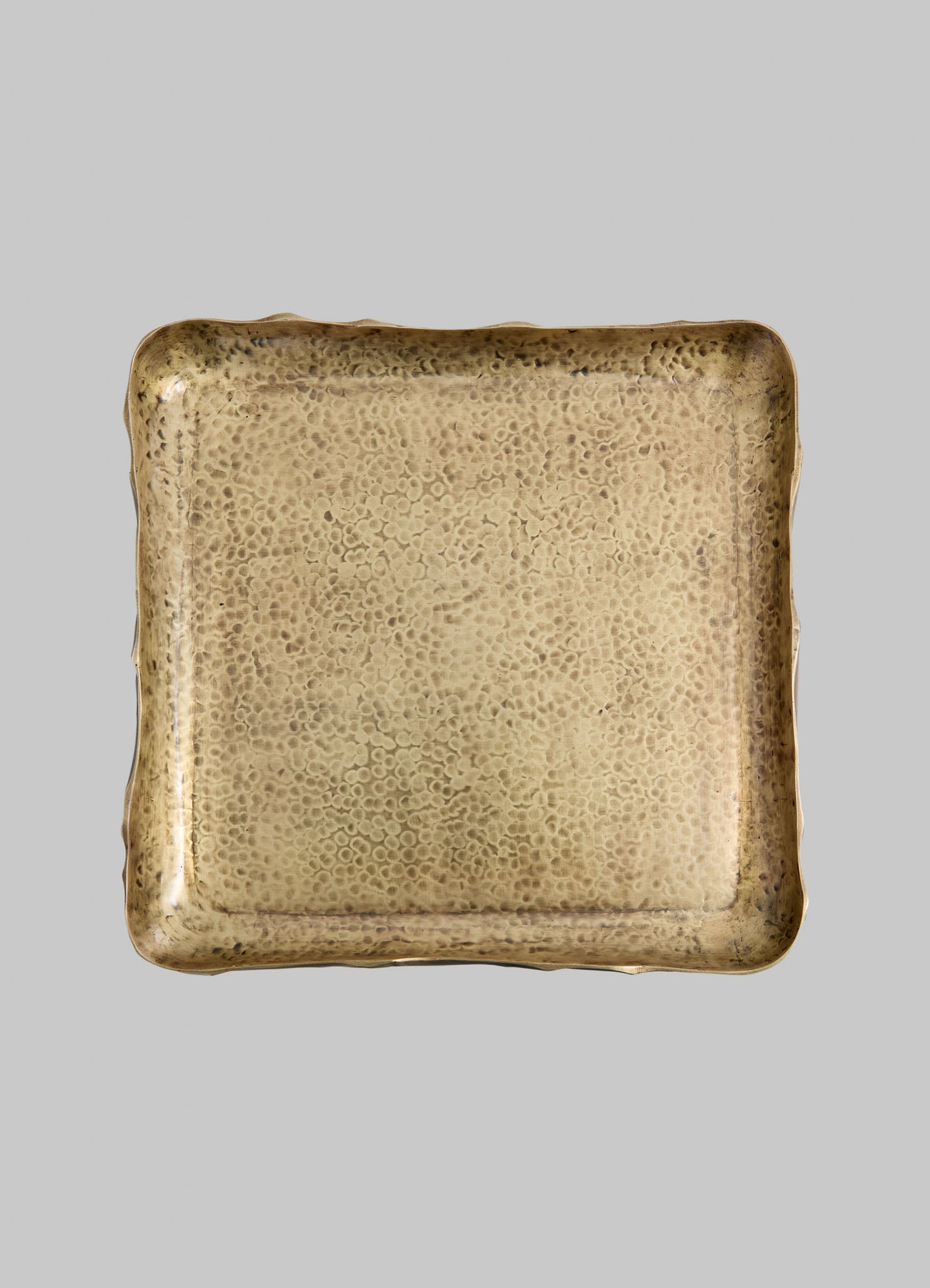 A square tray made of hammered metal with a gold finish, featuring rounded, slightly raised edges and a textured surface with small, circular indentations.