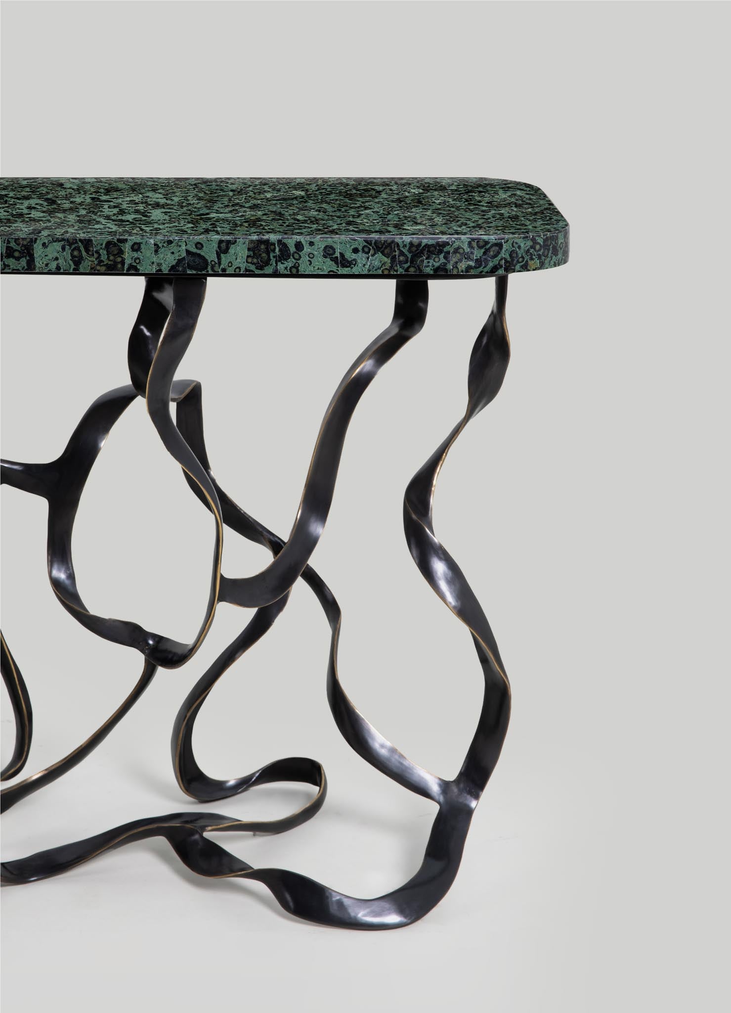 A table with a green and black patterned marble top and sculptural, twisted black metal legs with gold accents.