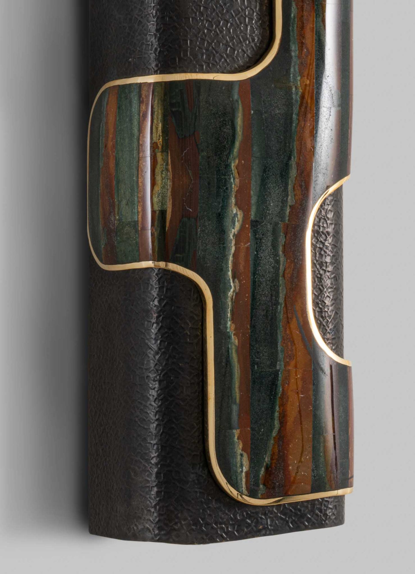 A decorative table with a textured black surface, featuring an inlaid stone top with green, brown, and orange tones and sinuous gold-colored metal accents.