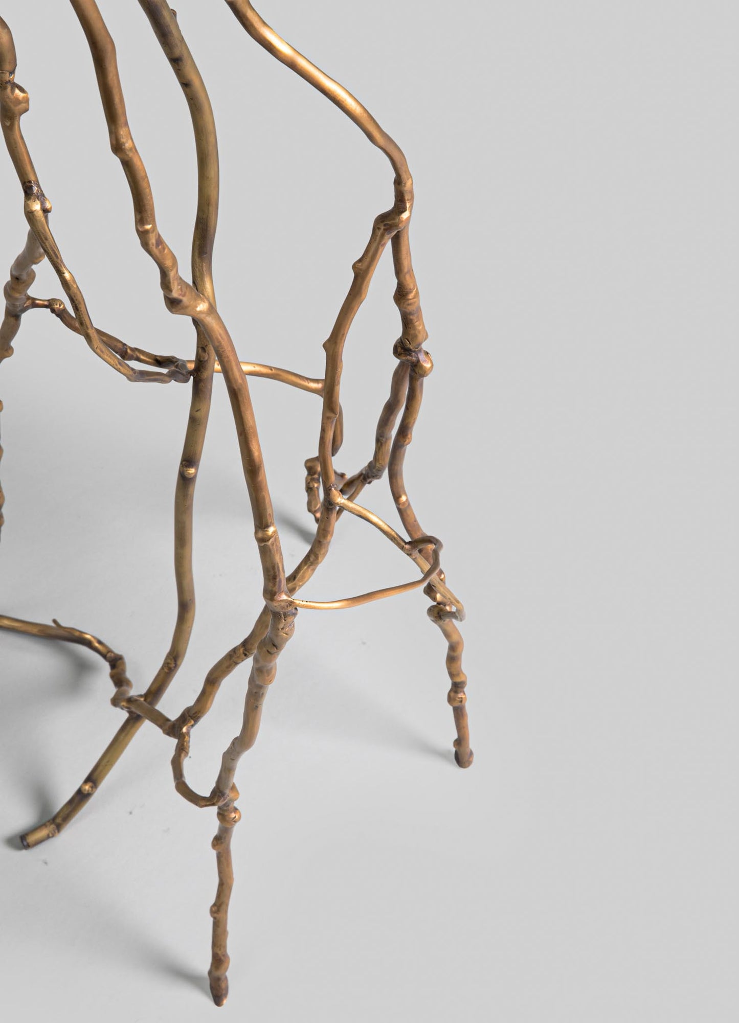 A sculptural side table or decorative stand made from twisted brass or metal branches with a metallic gold finish, featuring an organic, rustic design on a plain light background.