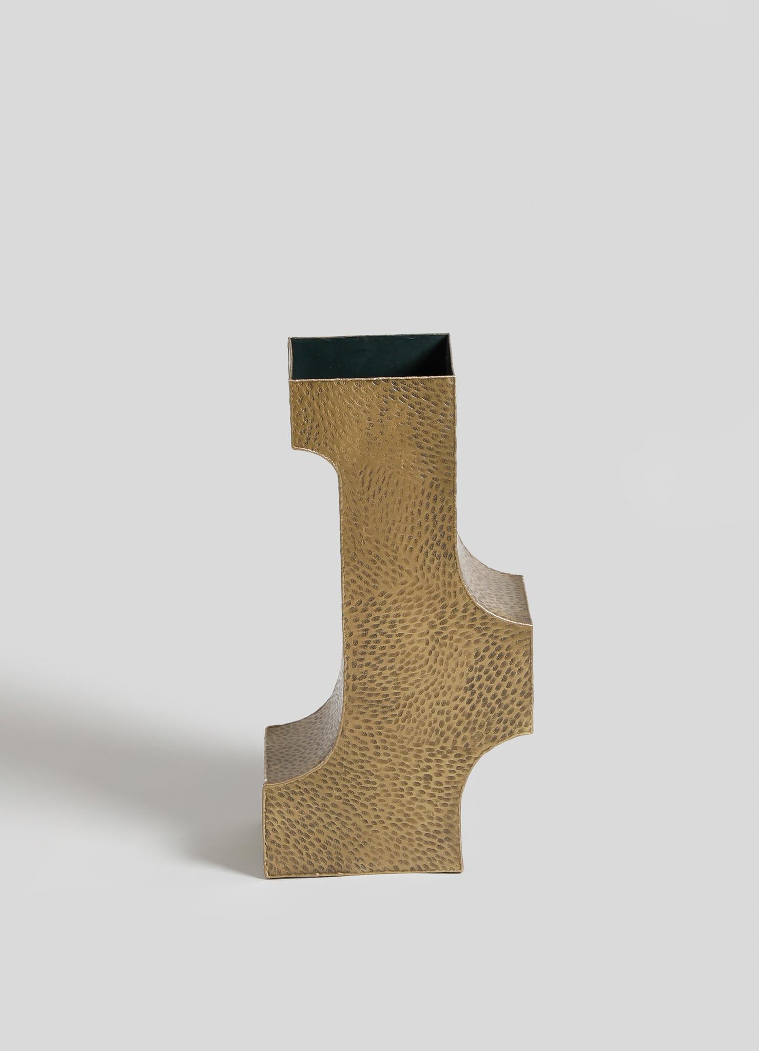 A gold-colored decorative object with a textured, hammered surface and a geometric, abstract shape, featuring a rectangular opening at the top.