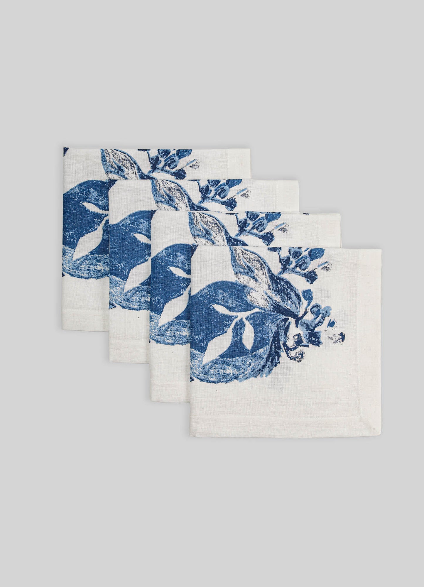 Linen napkins with a blue botanical print featuring leaves and small flowers on a white background, arranged in a fan shape against a light grey backdrop.