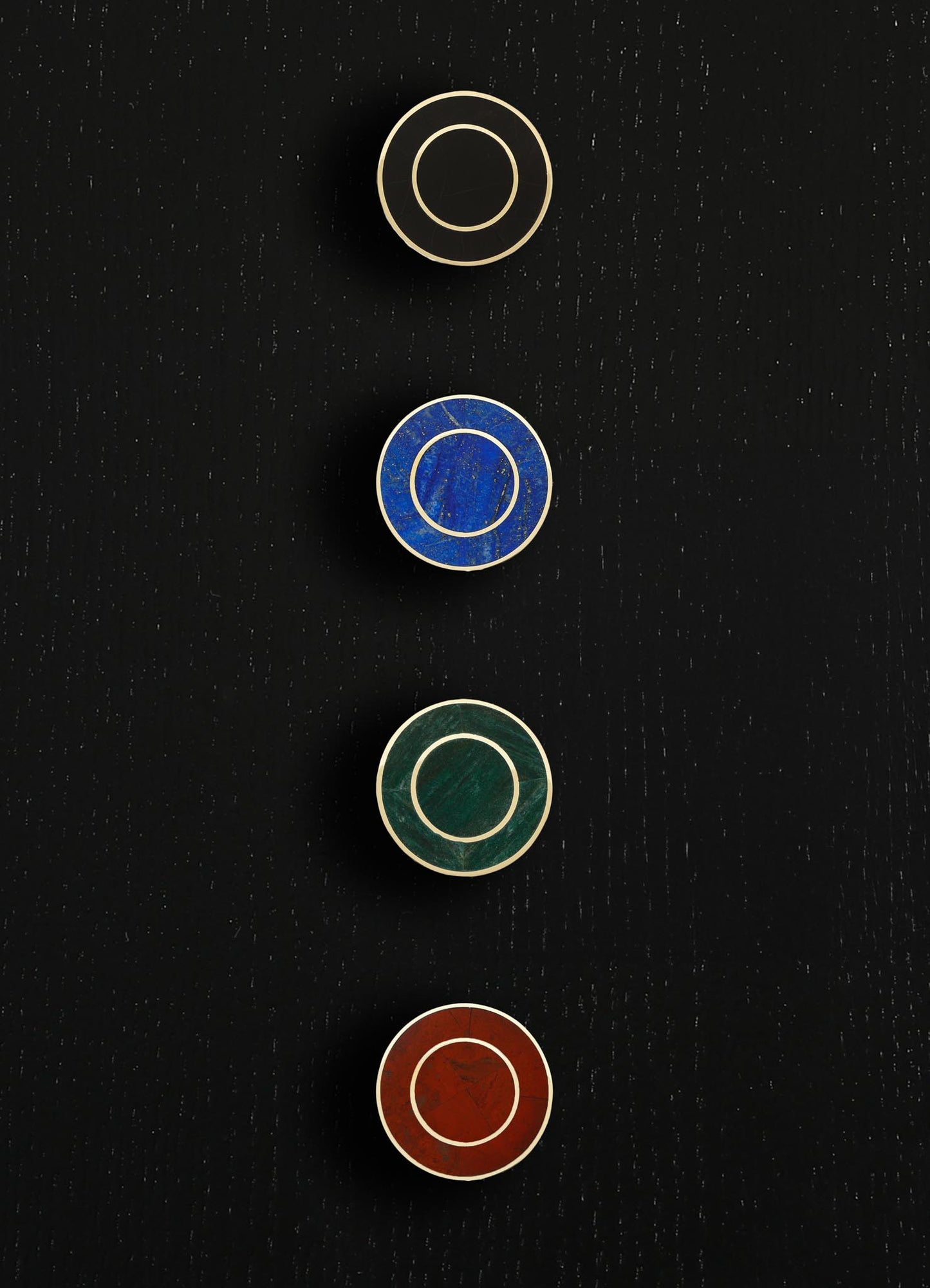 Circular wall hooks with colored stone discs in beige, blue, green, and red hues, bordered by metallic frames, mounted on a black wall surface.