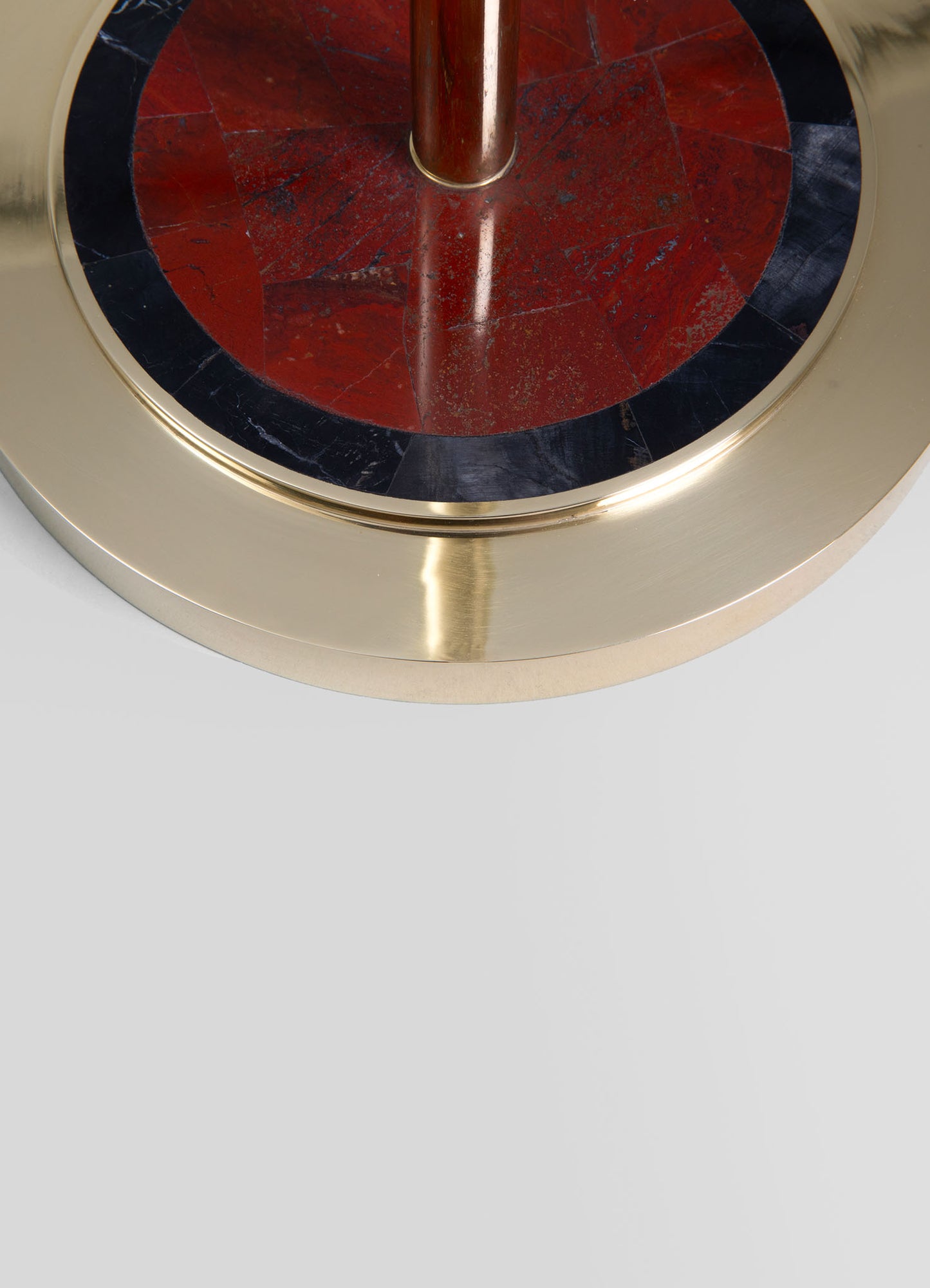 A round side table with a polished brass frame featuring a black and red marble top with geometric patterning, exuding a contemporary and luxurious style.