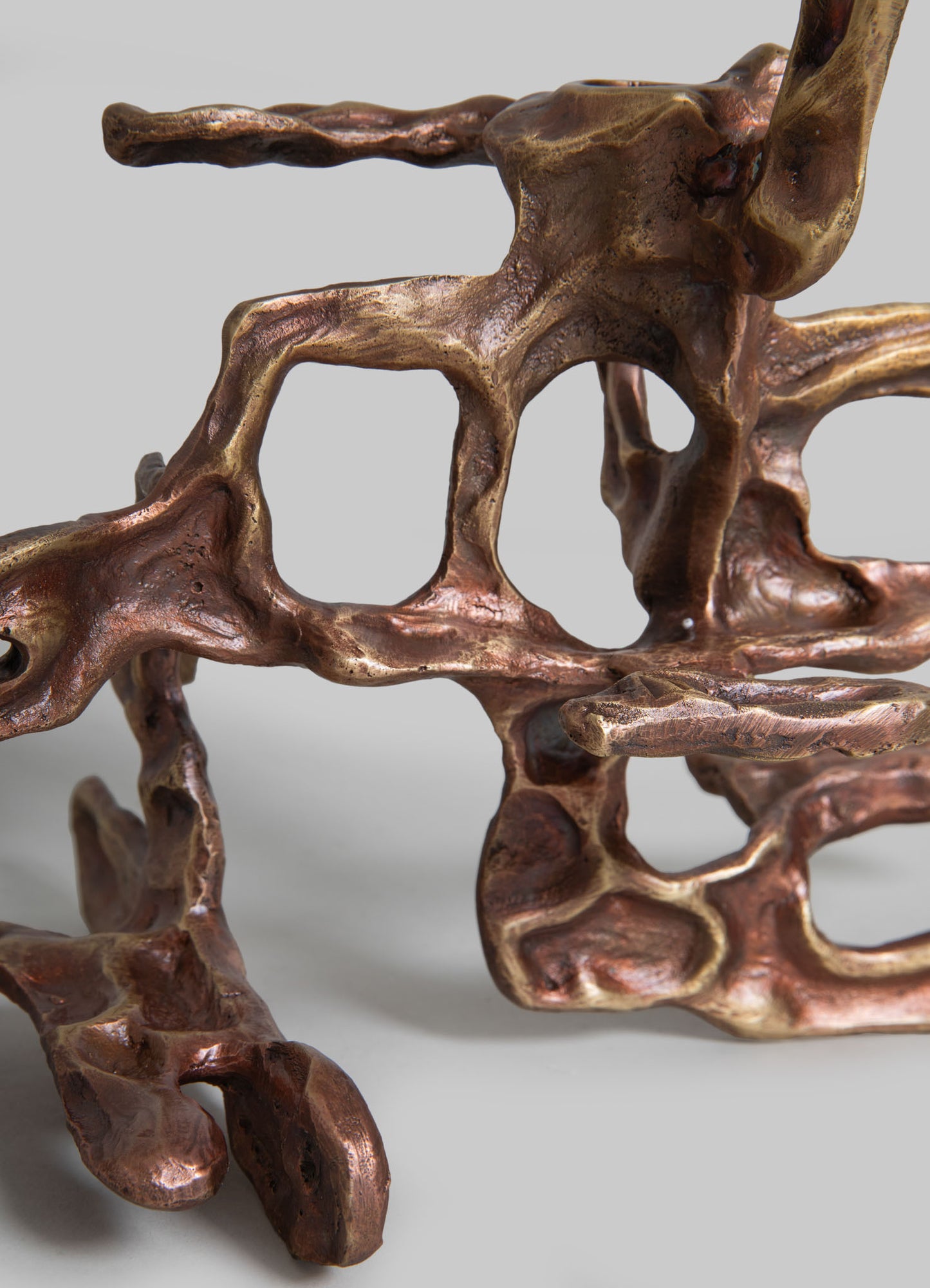 A decorative sculpture made of metal with a copper finish, featuring an abstract, openwork design with flowing, organic shapes and irregular patterns. The sculpture has a contemporary, artistic style with a textured surface.