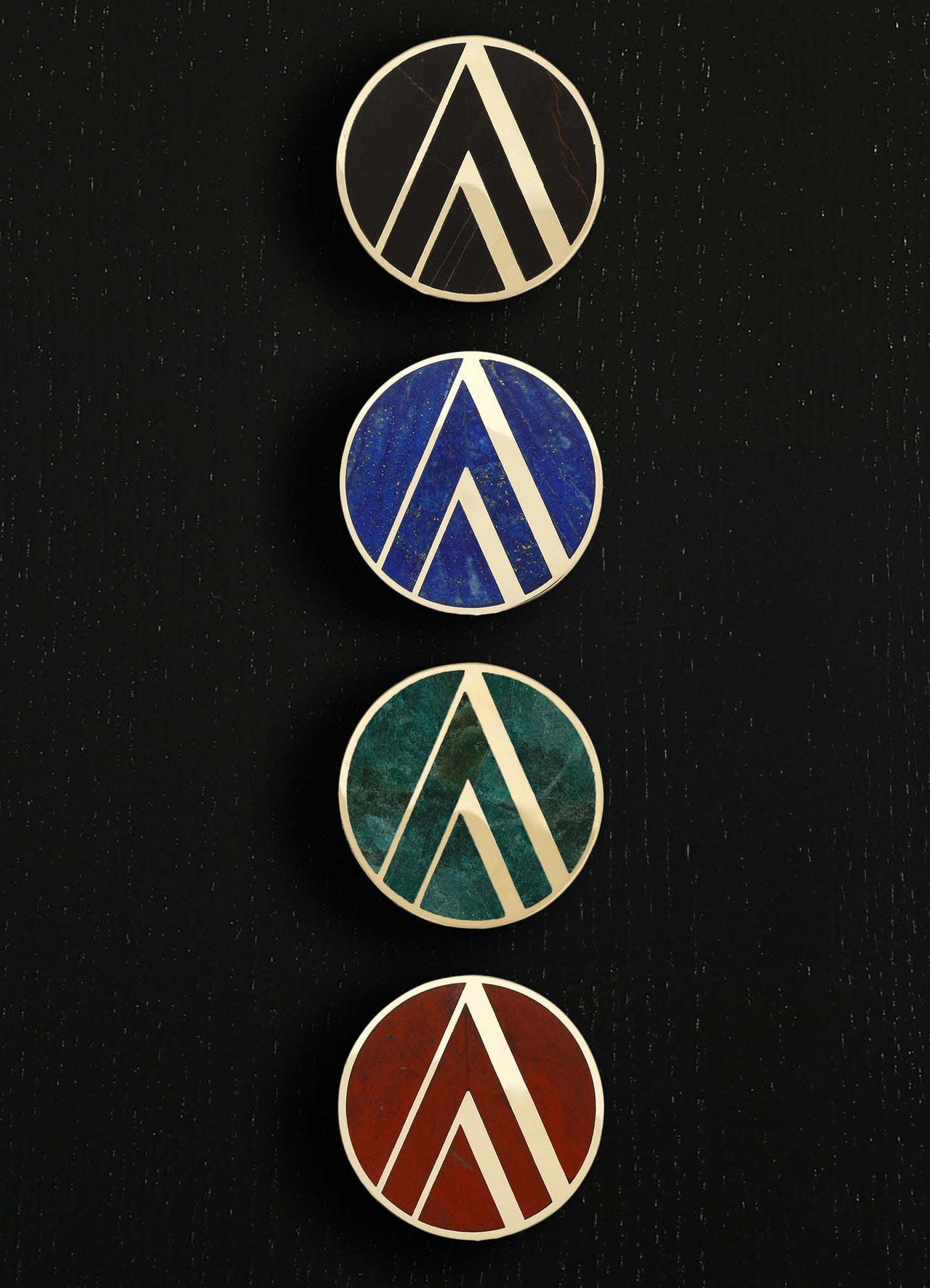 Set of four circular decorative wall plaques featuring geometric motifs with raised white borders, each with a different vibrant color background: black marble, blue, green, and terracotta. The style is modern and abstract, with a focus on bold color contrast and textured surfaces.