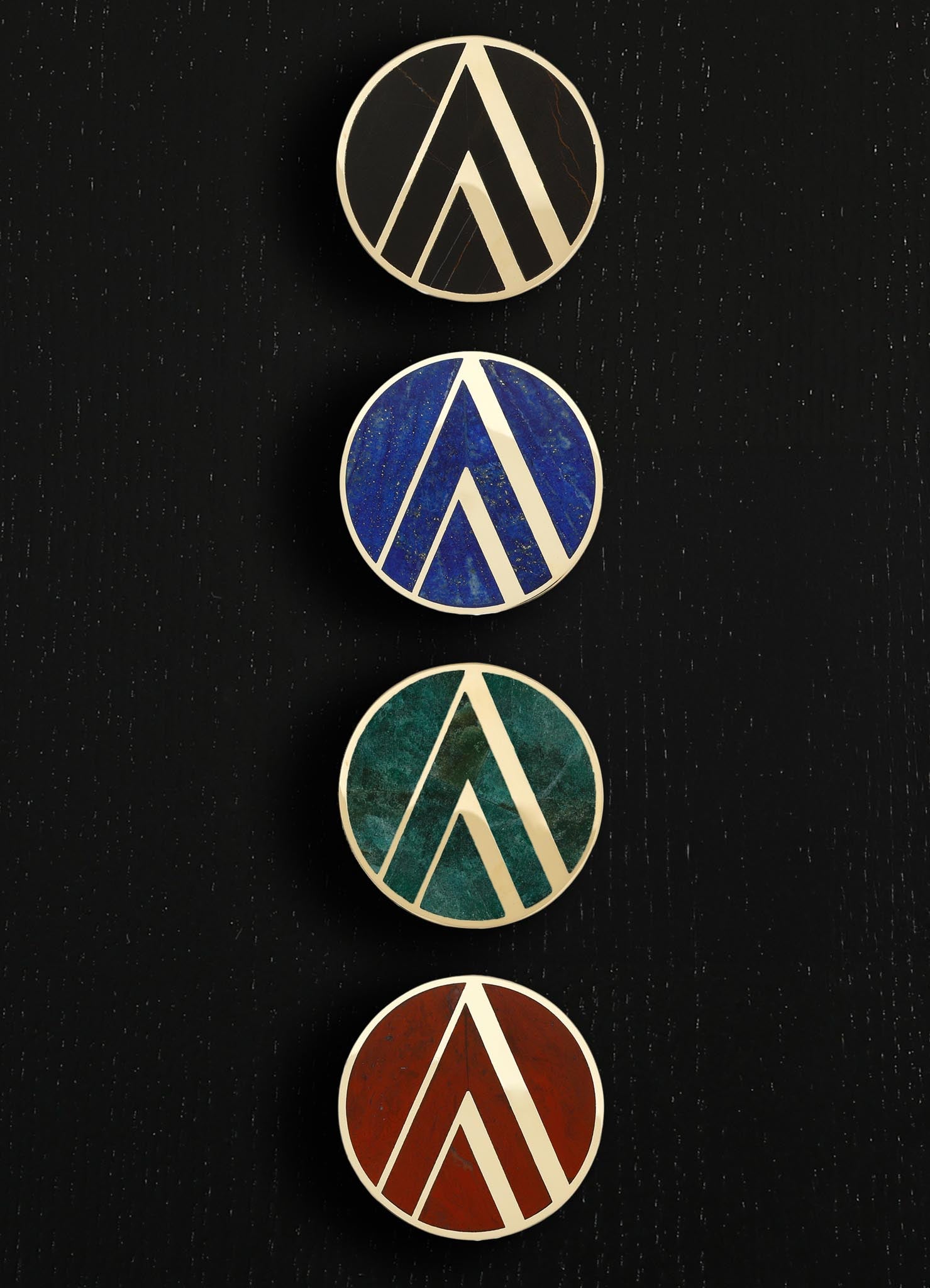 Set of four circular decorative wall plaques featuring geometric motifs with raised white borders, each with a different vibrant color background: black marble, blue, green, and terracotta. The style is modern and abstract, with a focus on bold color contrast and textured surfaces.