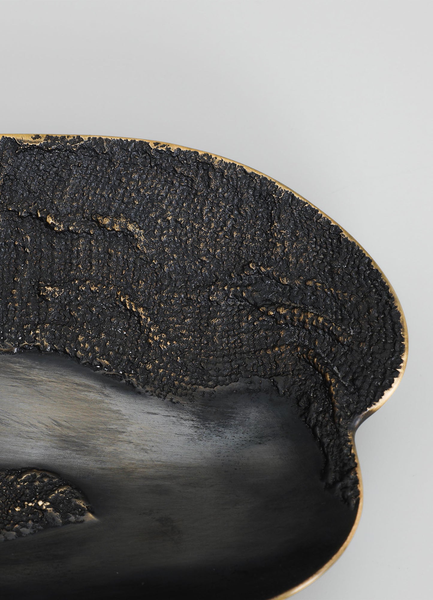 A black ceramic bowl with a textured, rough exterior surface and a smooth, matte interior finish, accented with a gold trim along the rim. The design combines rustic and contemporary styles with a focus on tactile contrast.