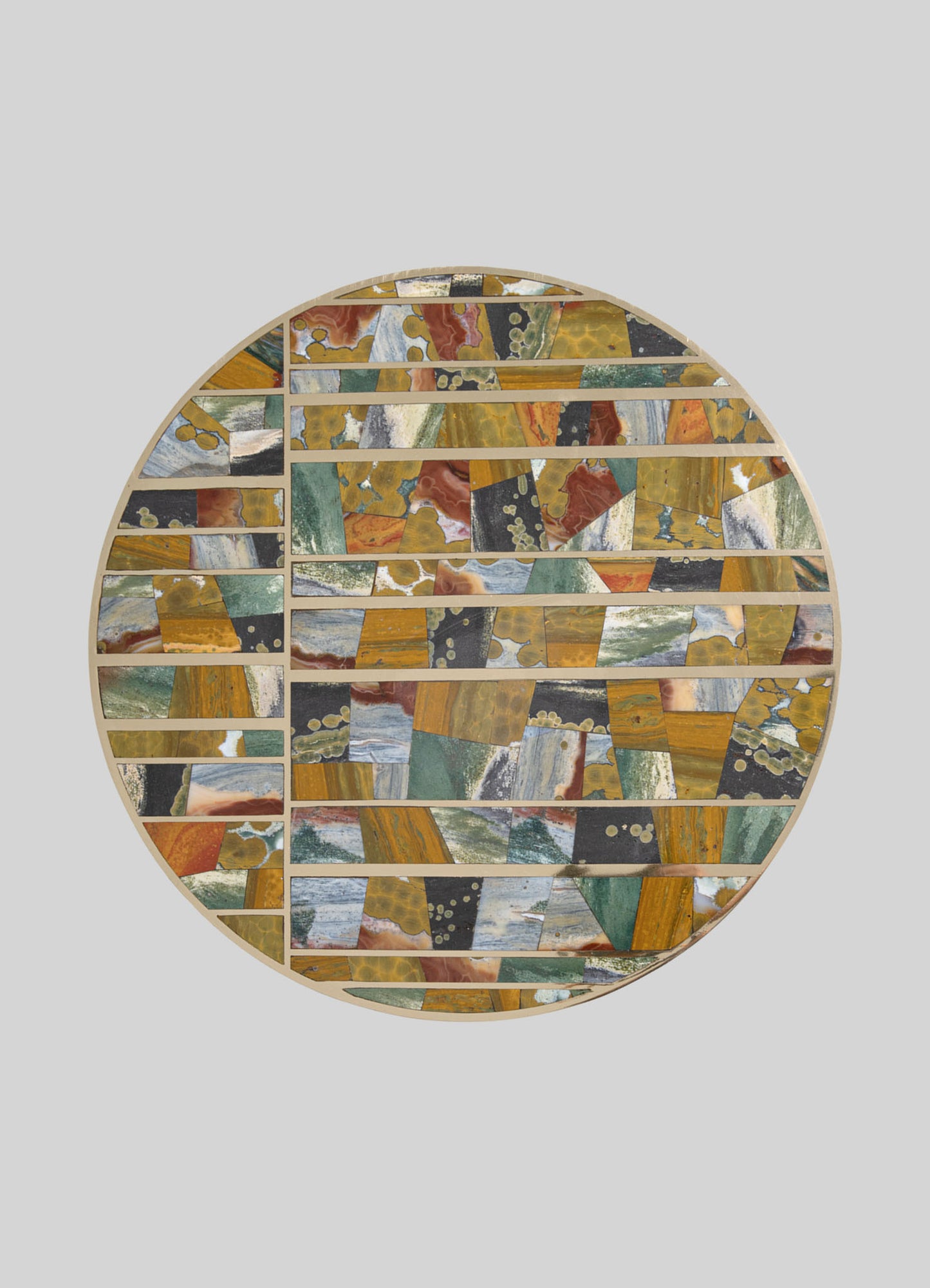 A round decorative tray featuring a mosaic pattern with irregular geometric shapes in warm tones of mustard yellow, rust, black, green, and white, bordered by a light wooden frame.